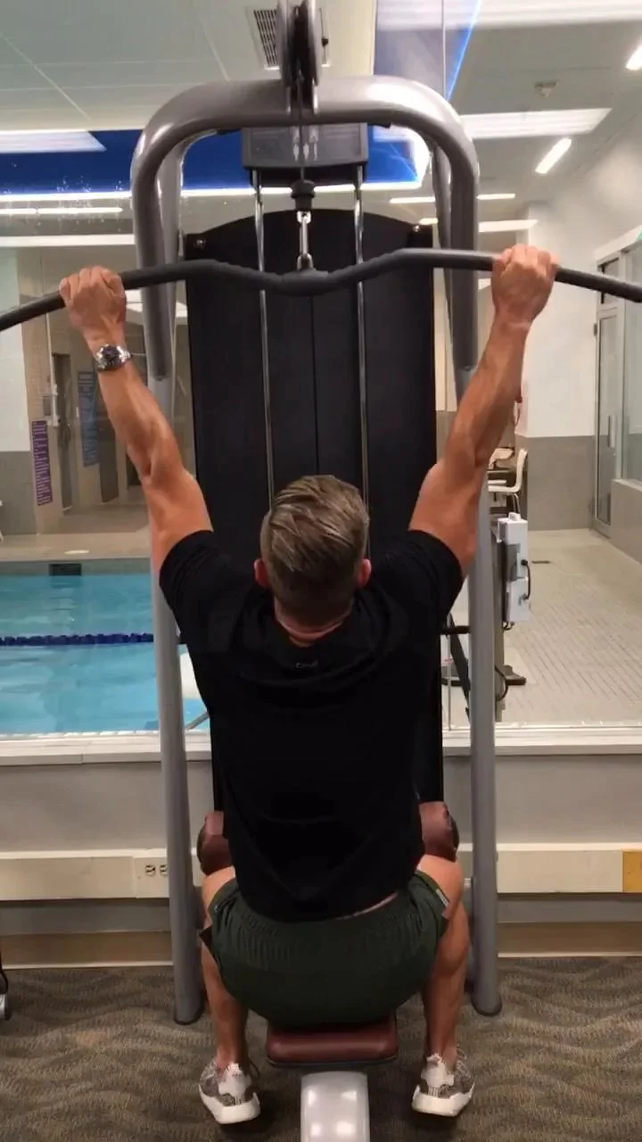 Man exercising with resistance bands in a gym, surrounded by dumbbells and greenery.