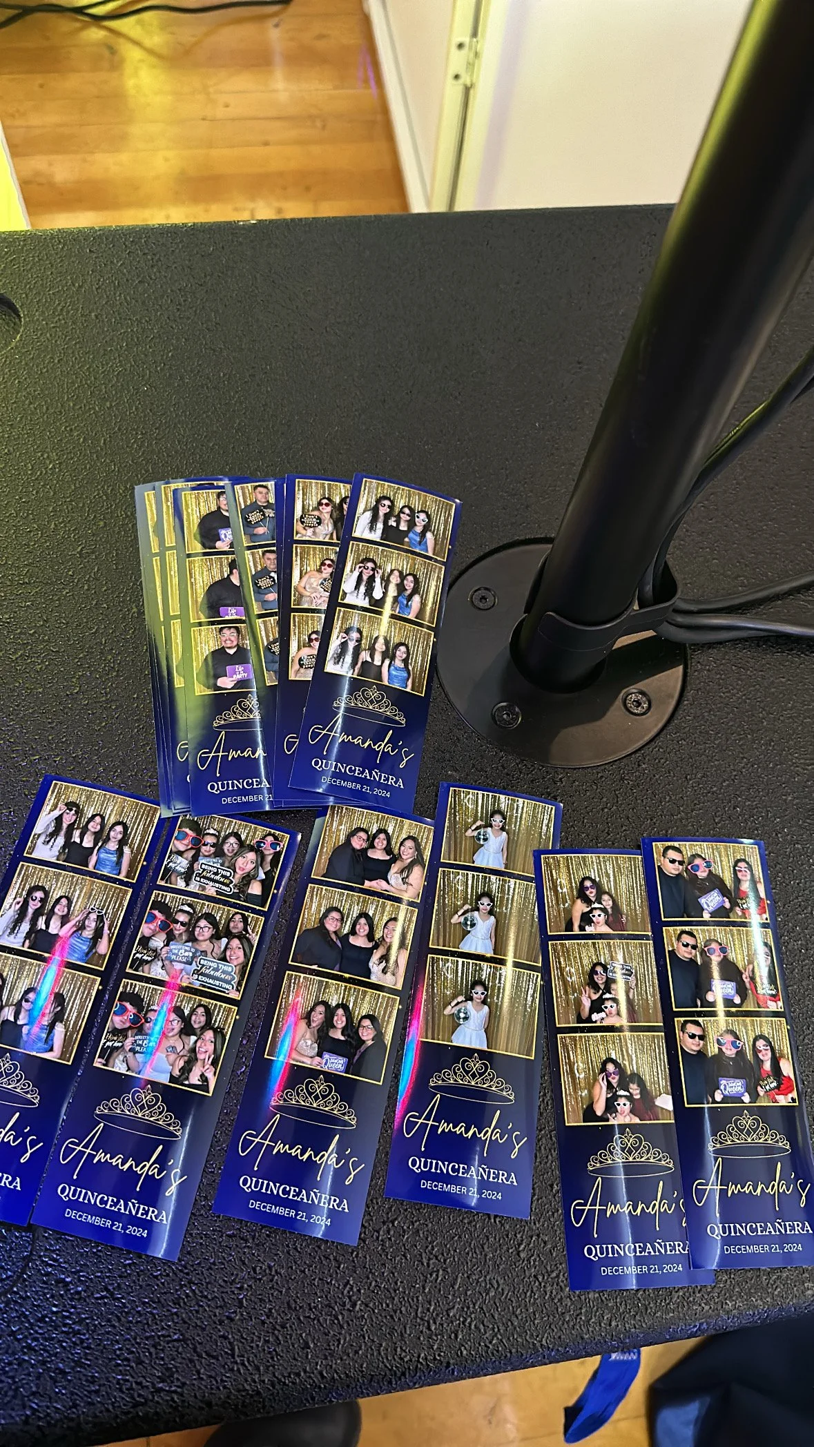 Photo booth photo strips from a quinceañera party with the name 'Amanda' and the date December 21, 2024, showing guests in various poses and costumes, laid out on a black table at an event.