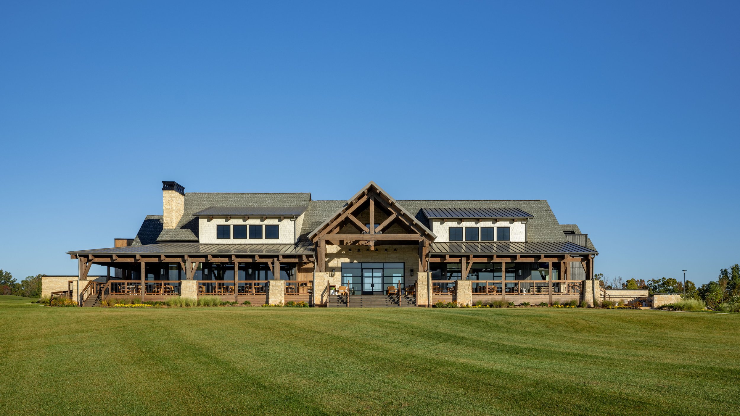 Large modern house with stone and wood exterior, set on a well-maintained green lawn under a clear blue sky.