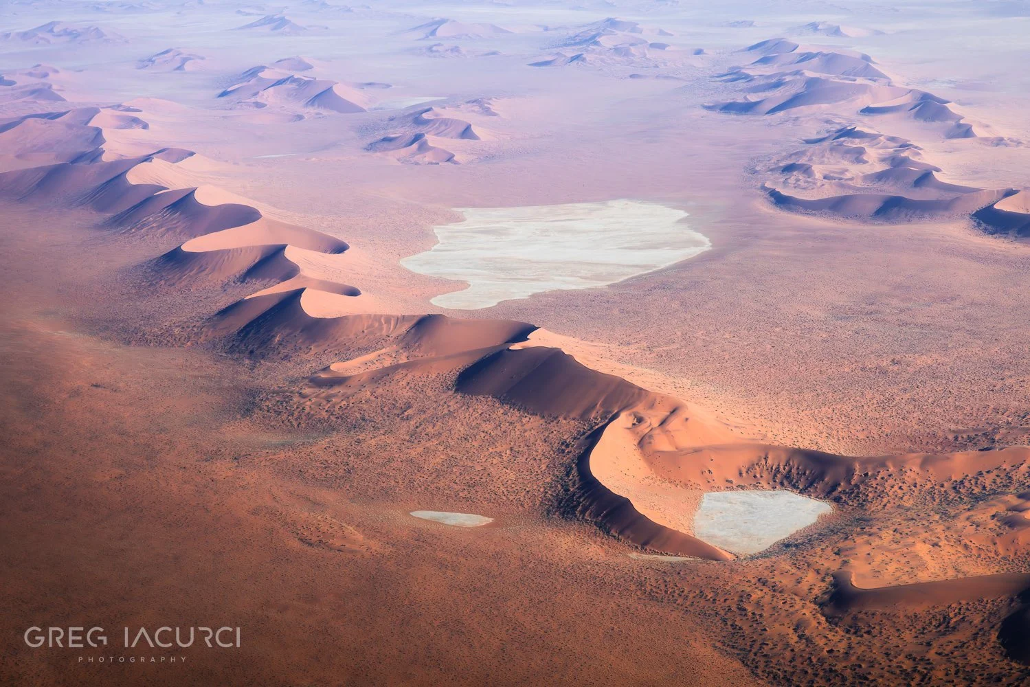 In an aerial shot, dunes of red desert sand stretch to horizon.