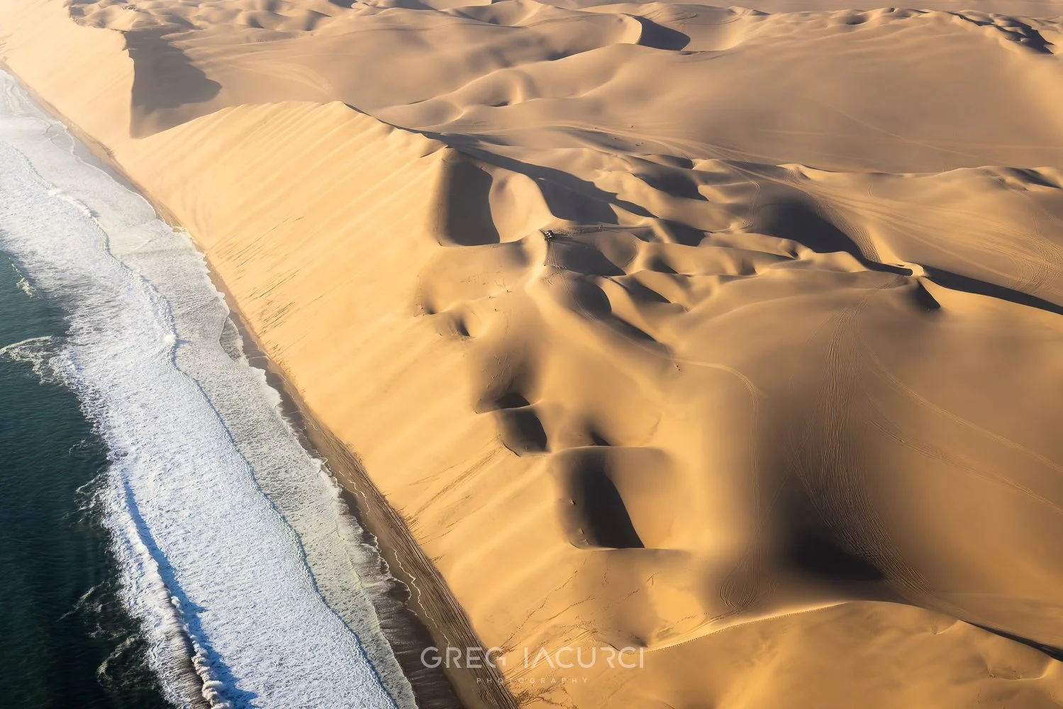 Tall golden desert sand dunes meet the ocean.