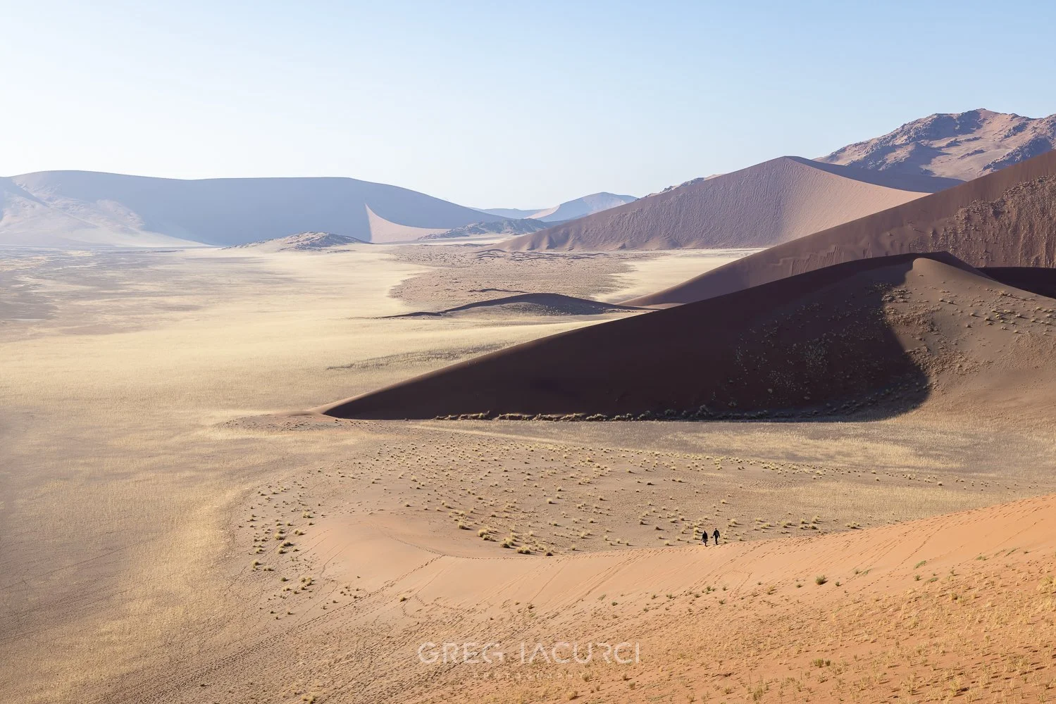 Two people walk amid towering sand dunes in desert.