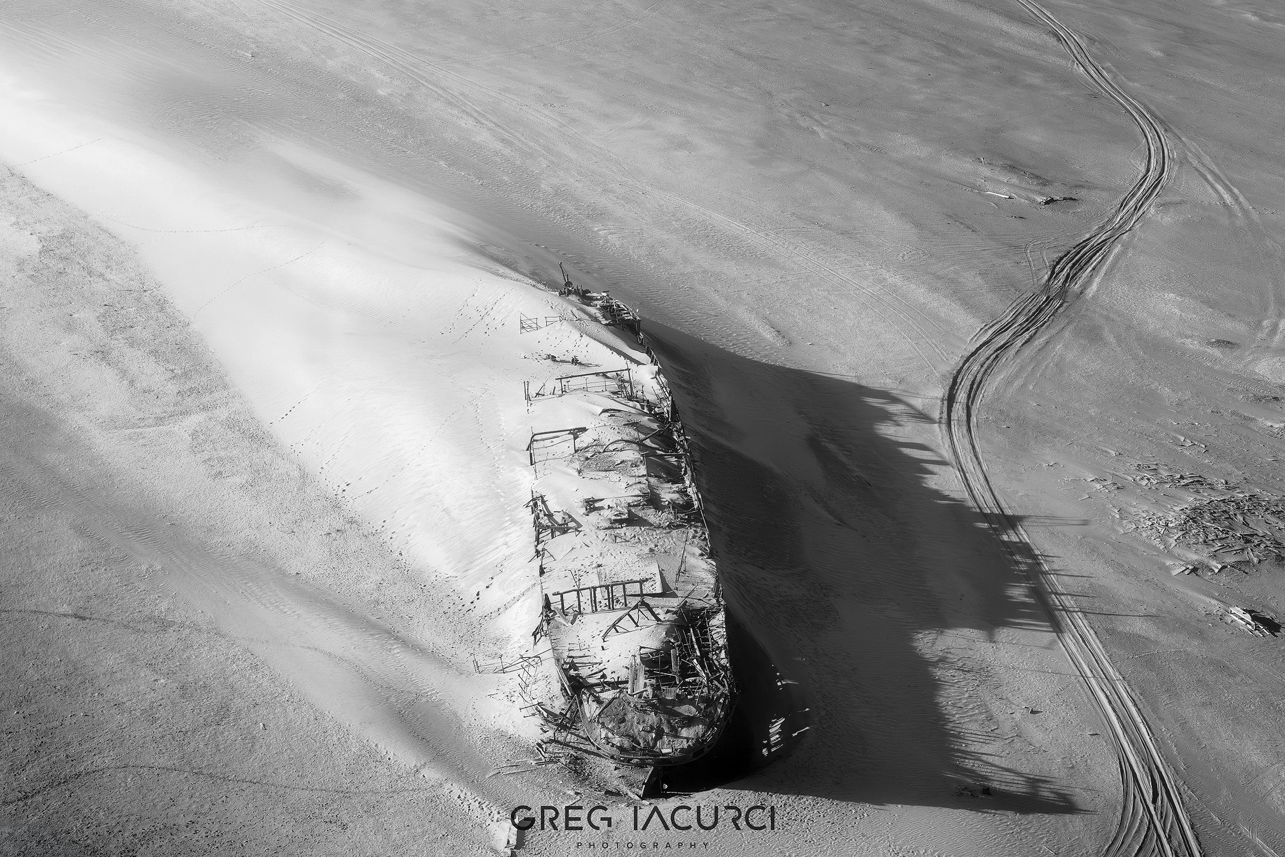Aerial view of rusted ship covered in desert sand dunes.