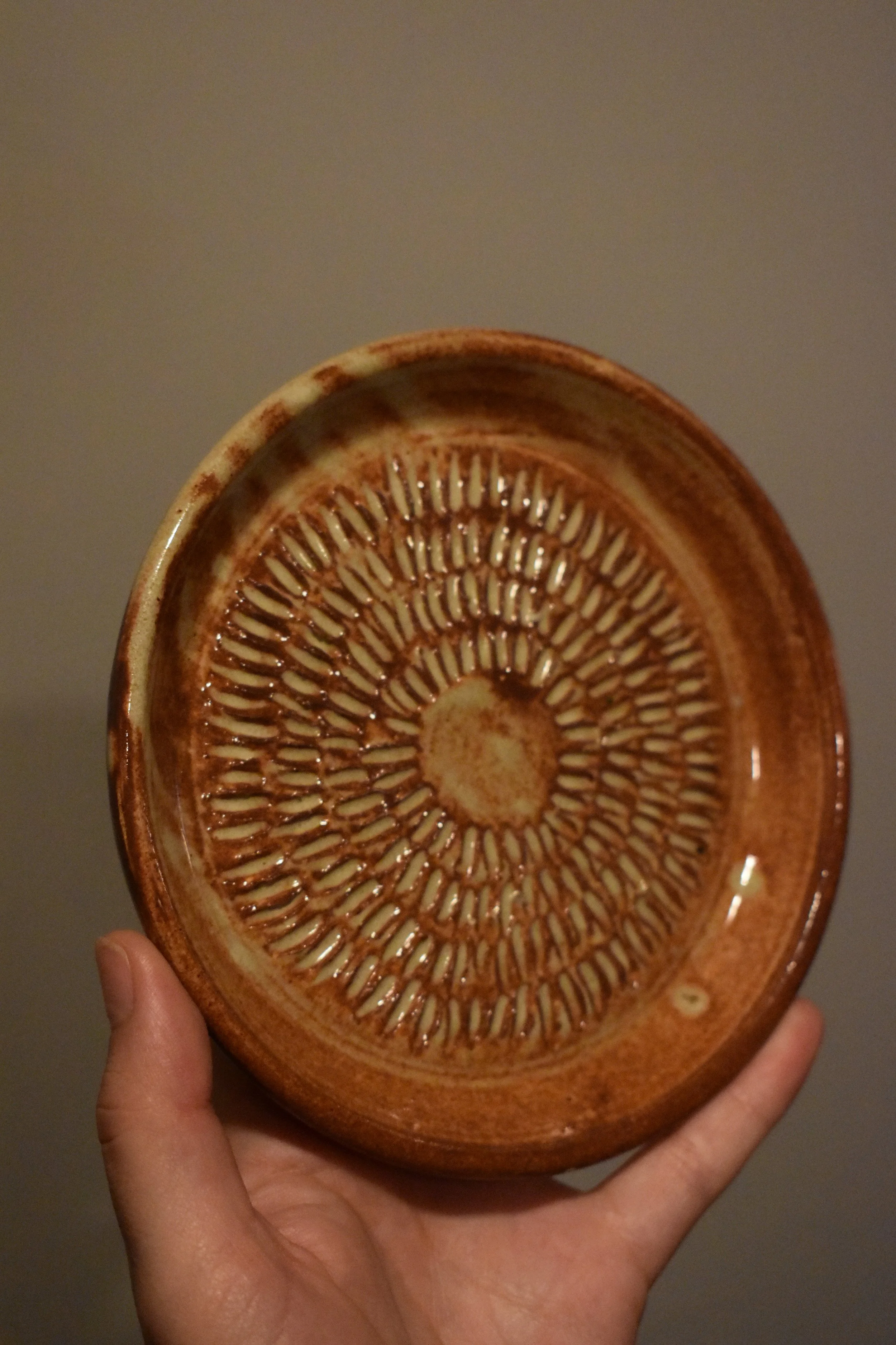 A hand holding a brown ceramic bowl with intricate textured design on the interior surface.