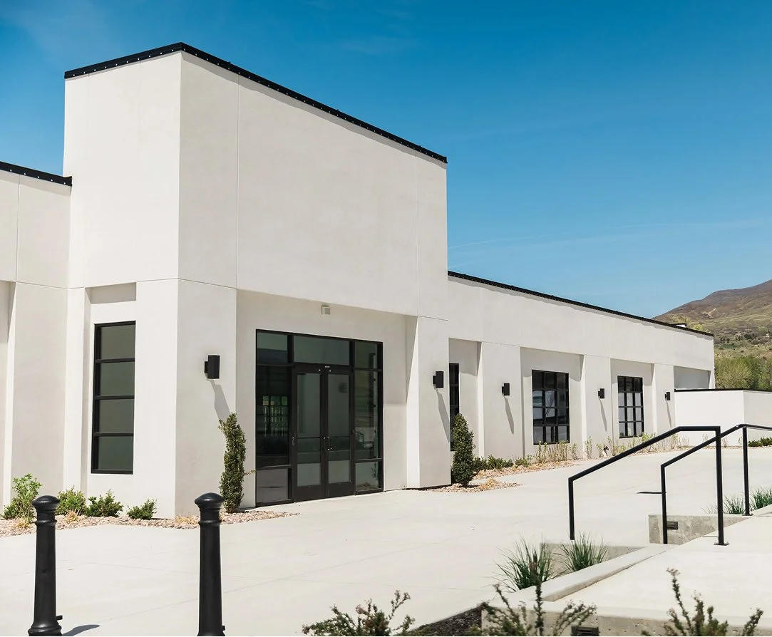 Modern white building with black accents under a clear blue sky and distant hills.