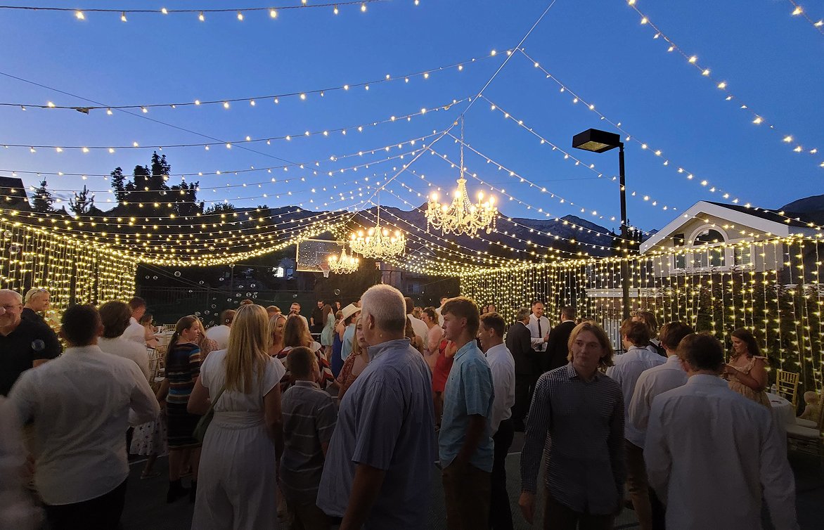 People at an outdoor evening party under string lights and chandeliers