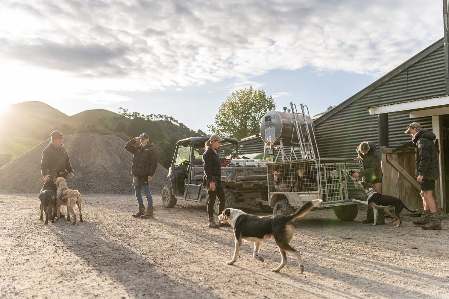 People with dogs and an ATV on a farm with hills in the background.