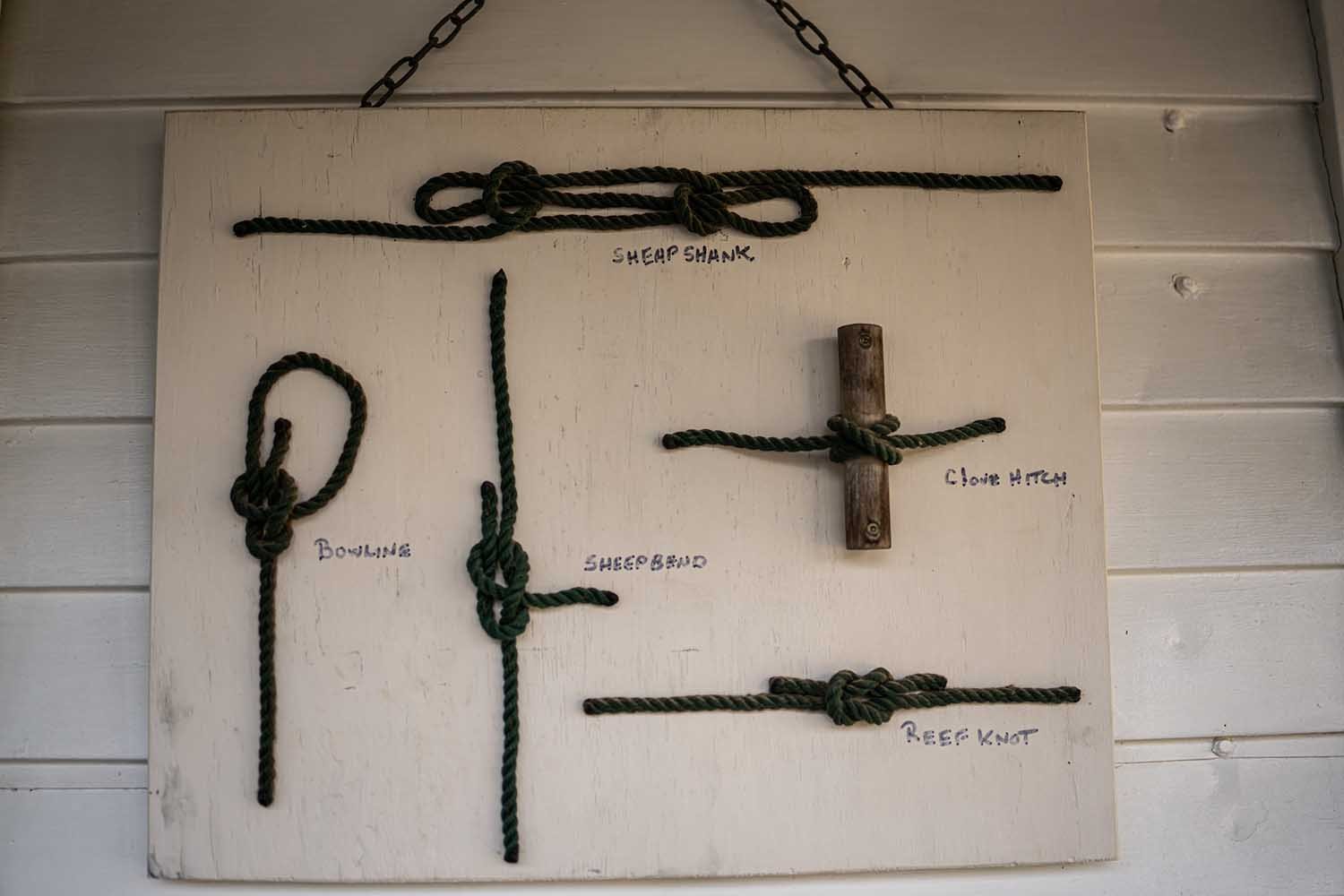 Board displaying various knots, including bowline, sheep shank, clove hitch, sheep bend, and reef knot, with labels.