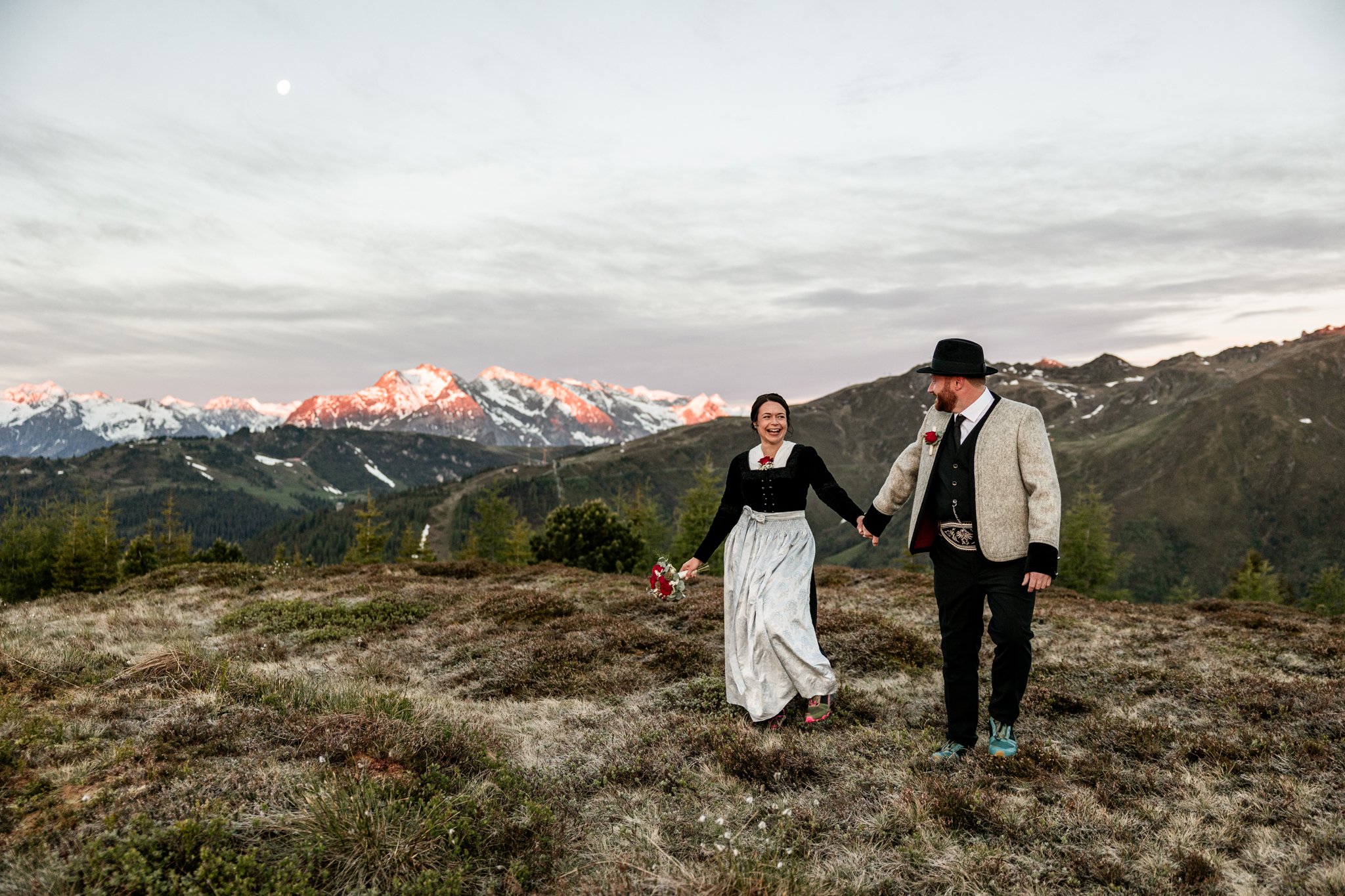 Bräutigam und Braut lachen beide, halten sich Hand in Hand und laufen dem Sonnenaufgang entgegen. 