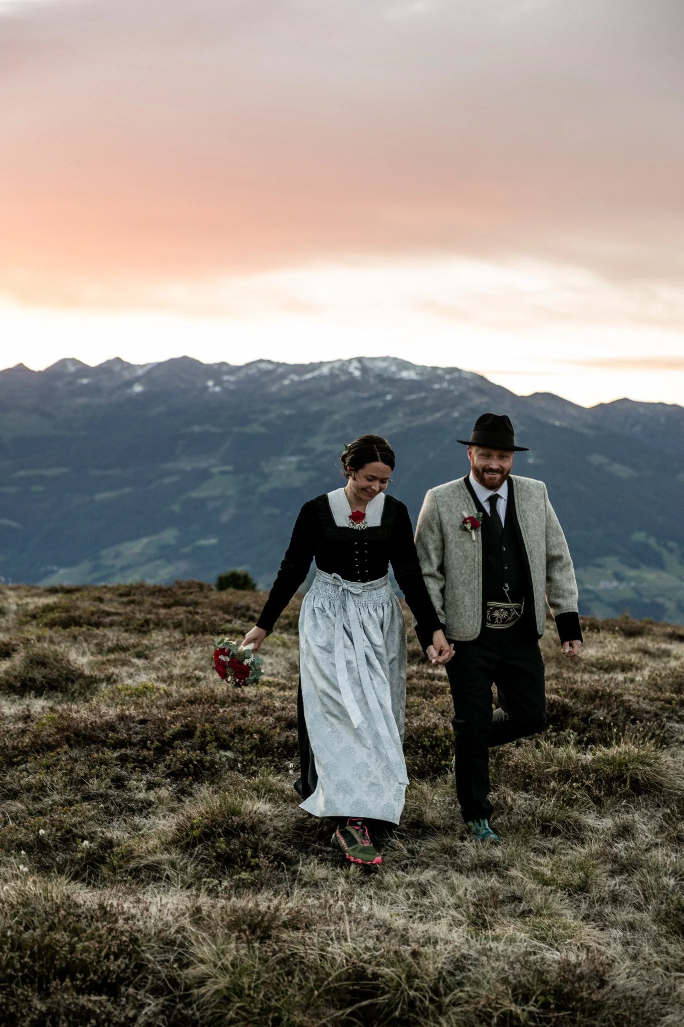 Glückliches Brautpaar, gekleidet in traditioneller Zillertaler Tracht, spaziert auf dem weichen Boden in den Bergen oberhalb von Mayrhofen