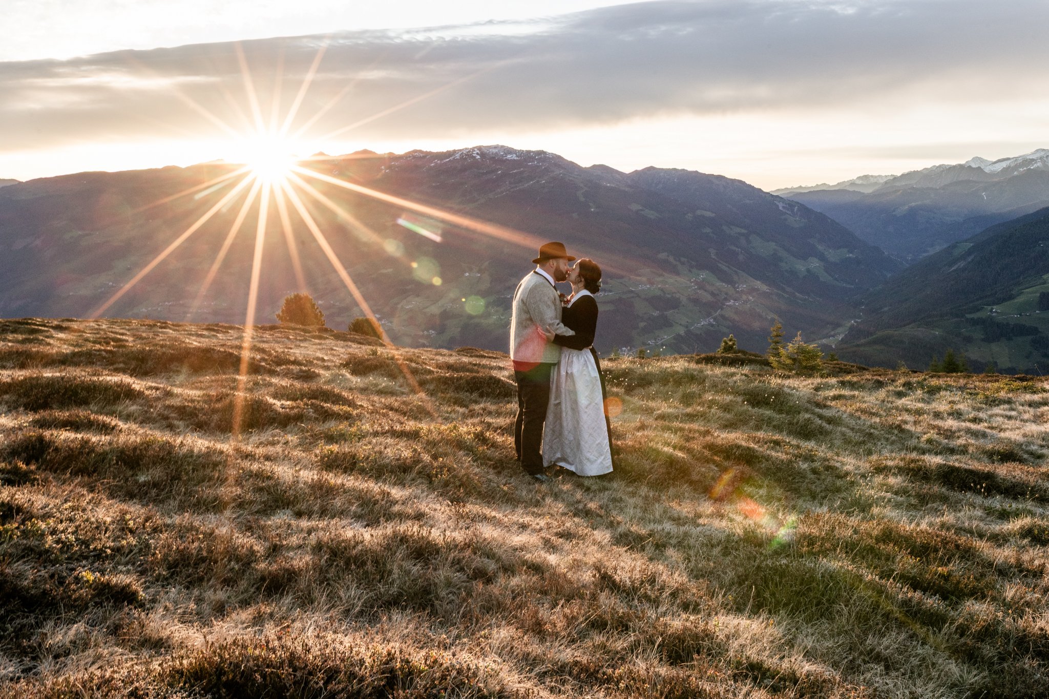 Mann und Frau küssen sich, währen die Sonne über den Bergen in Zell am Ziller und Rohrberg aufgeht. Hochzeit am Berg im Zillertal. 
