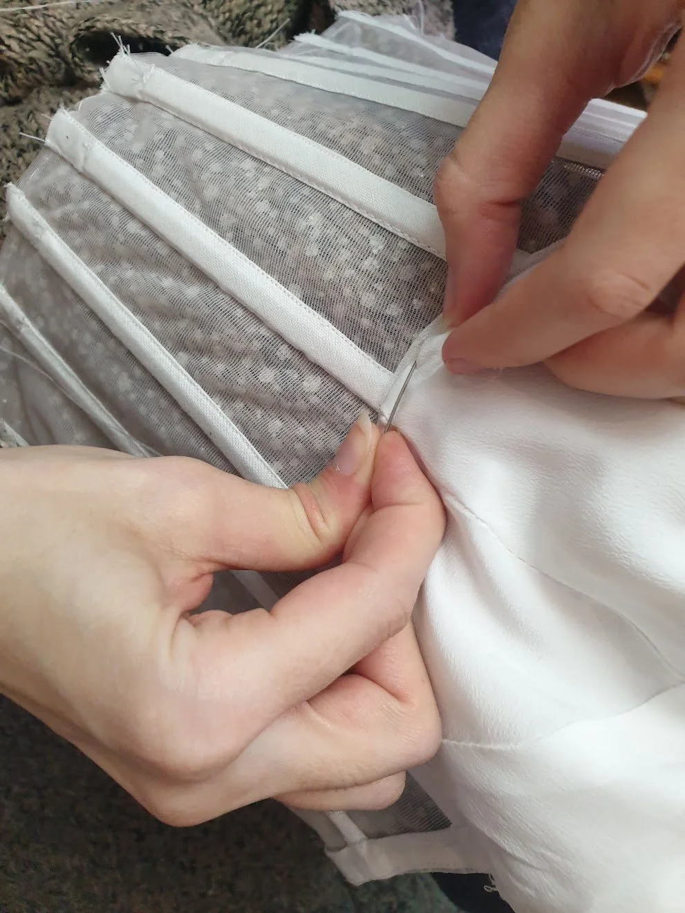 Cups lining pinned and being hand-stitched from the inside of a see-through corset. This delicate process ensures a seamless and secure fit.