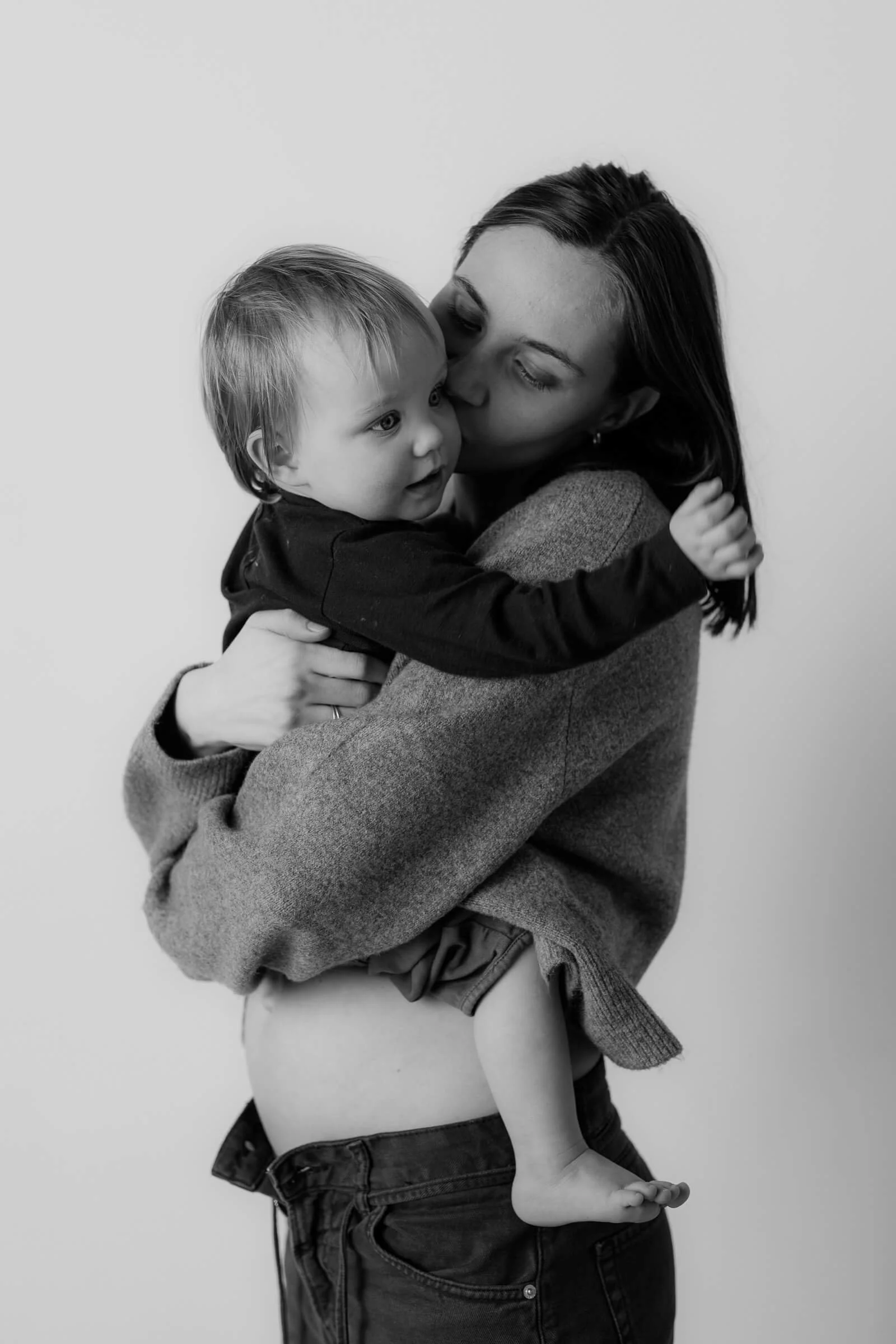 Black and white photo of a woman holding a young child, sharing a kiss on the cheek.