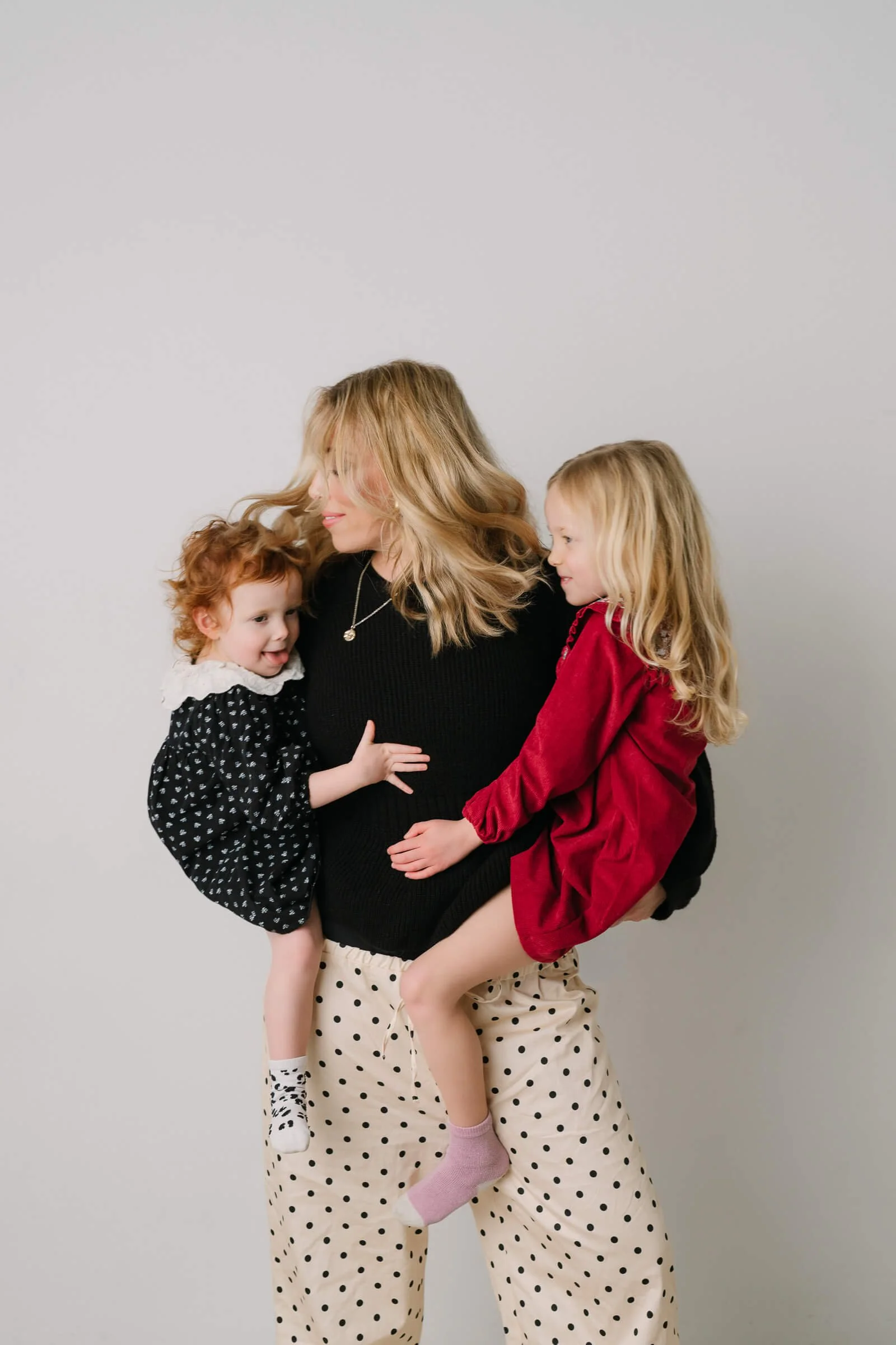 A woman holding two young girls, one on each side, against a plain white background.