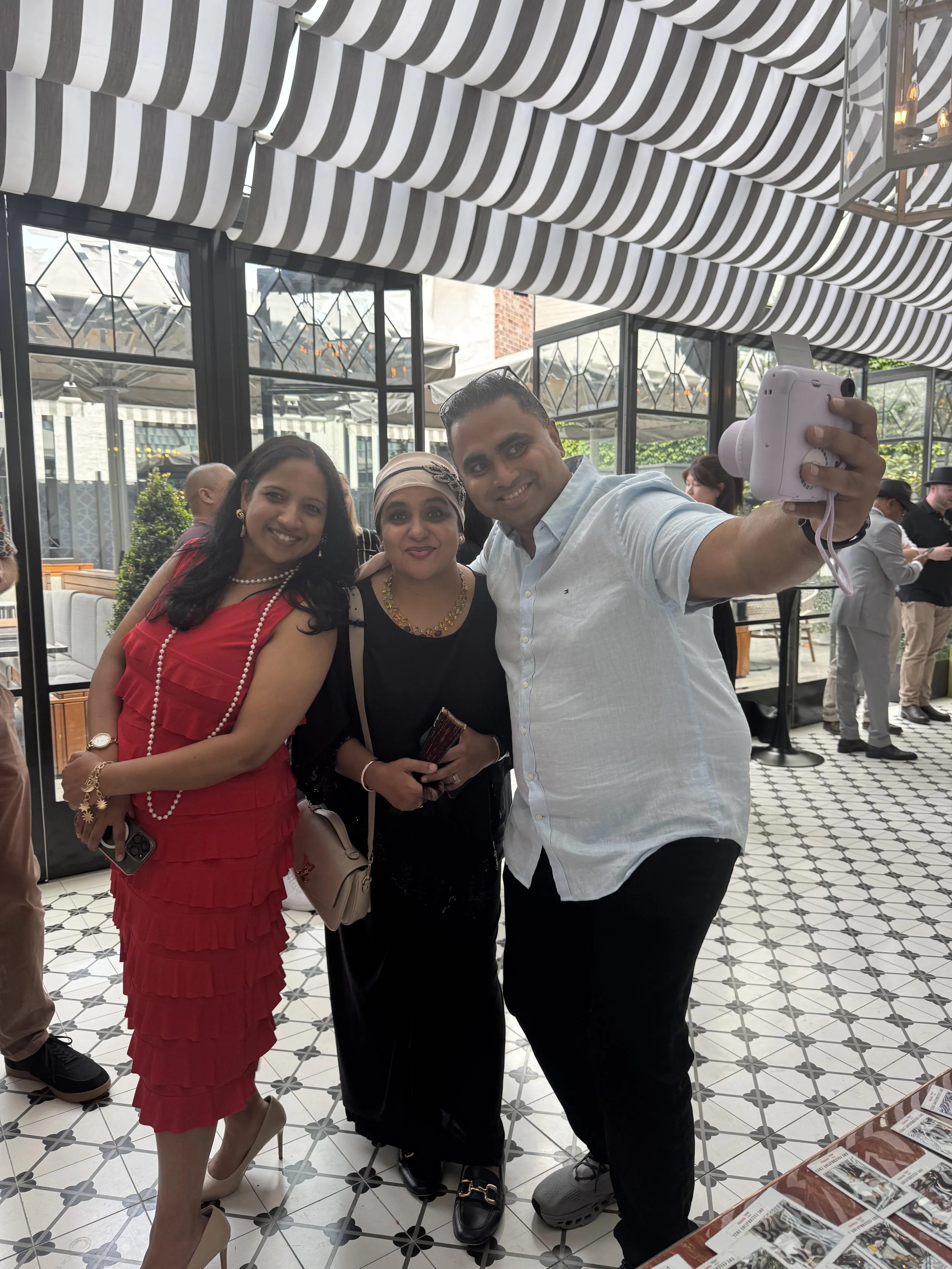 Group of three ethnically diverse people taking a selfie in a restaurant, with patterned flooring and striped awning overhead.