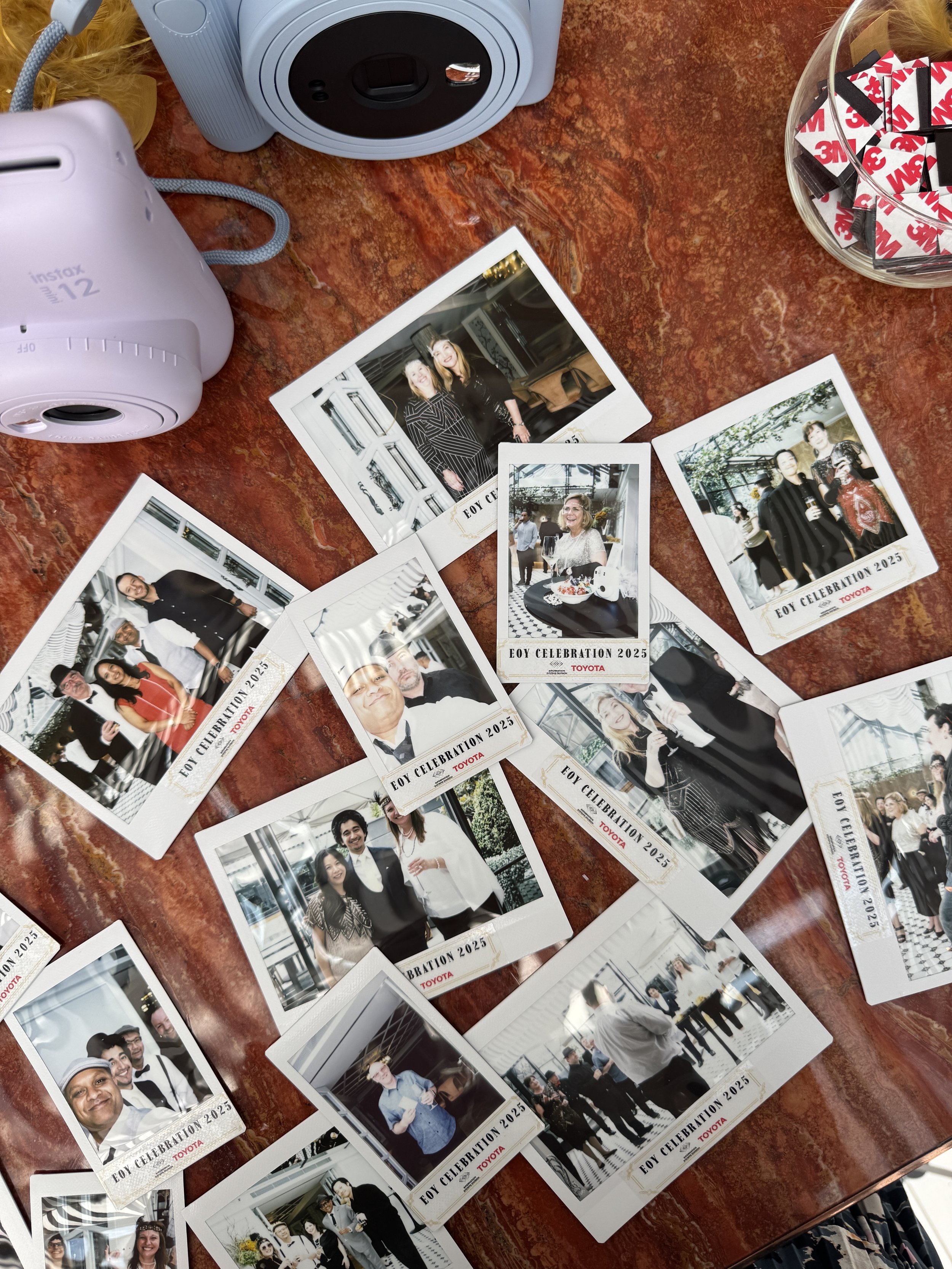 Photographs from a celebration event featuring various groups of people, some dressed formally, on a wooden table with a camera, a bowl of adhesive stickers, and a yellow dusting brush.