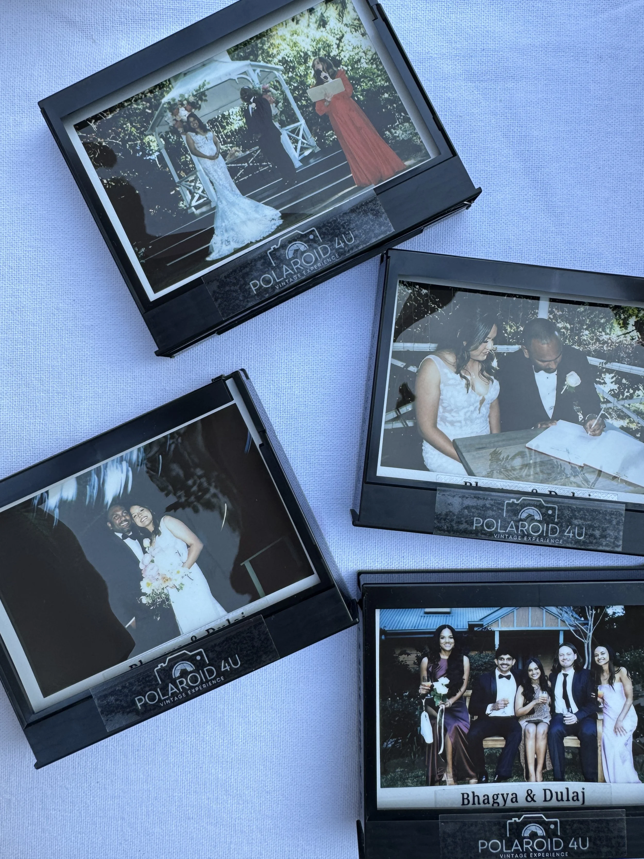 Four Polaroid photos displayed on a light blue surface, capturing moments from a wedding, including the bride and groom, wedding ceremony, and a group photo with guests.