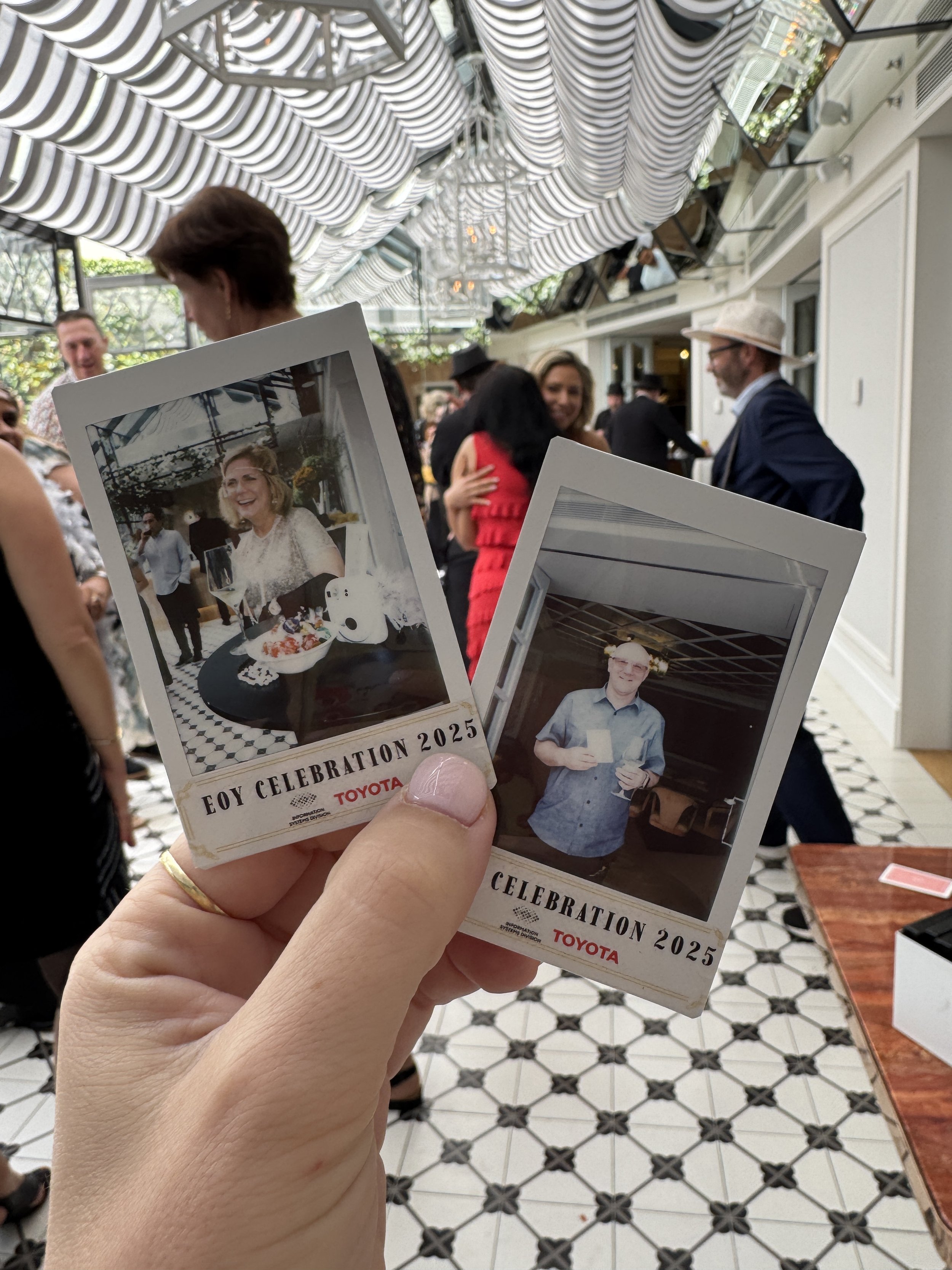 Polaroid photos held in a person's hand at a celebration event with people dancing and chatting in the background.