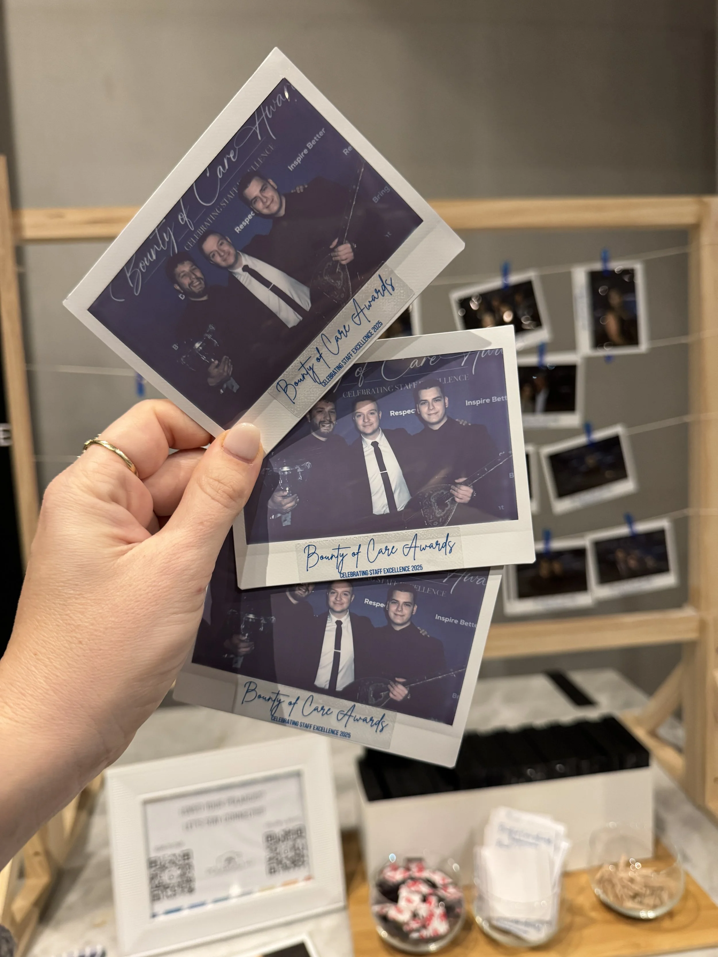 Three printed photographs for the Bounty of Care Awards held in 2023, with a background display of installed photographs on a wire grid.
