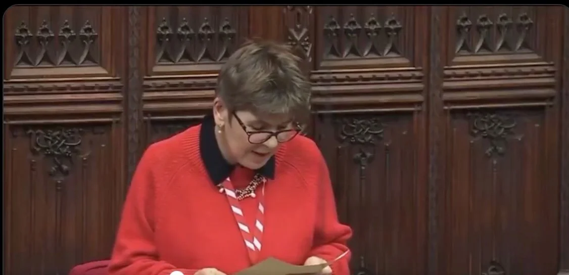 Person reading a document in an ornate wooden room, wearing glasses, a red sweater, and striped tie.
