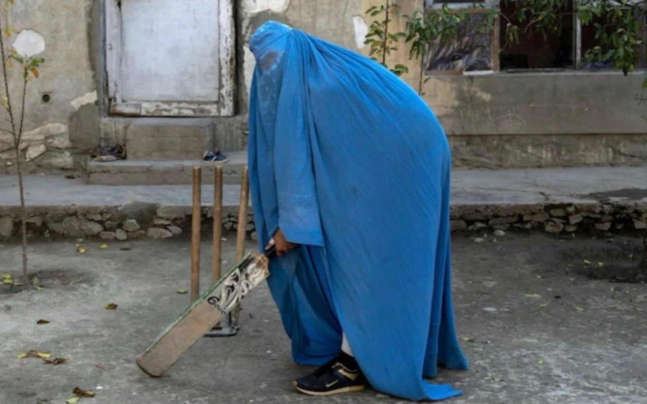 Person in a blue burqa playing cricket in a courtyard