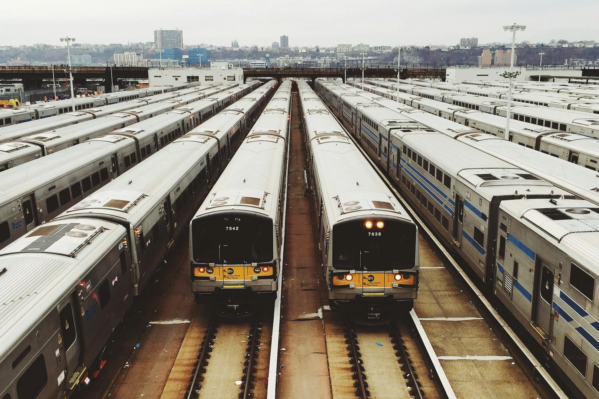 Multiple train cars parked in a rail yard with a city skyline in the background.