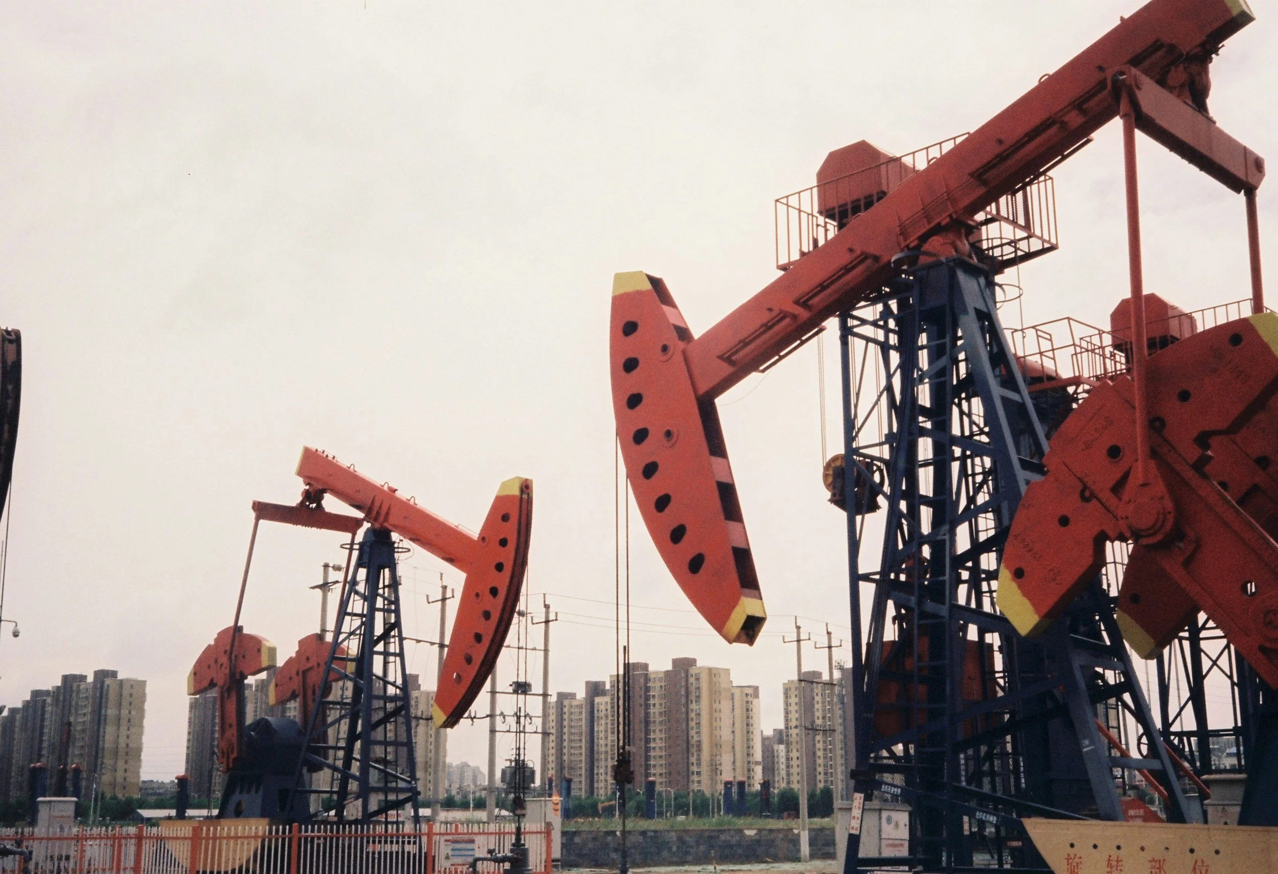 Oil pumps in an outdoor oil field with a city skyline in the background.