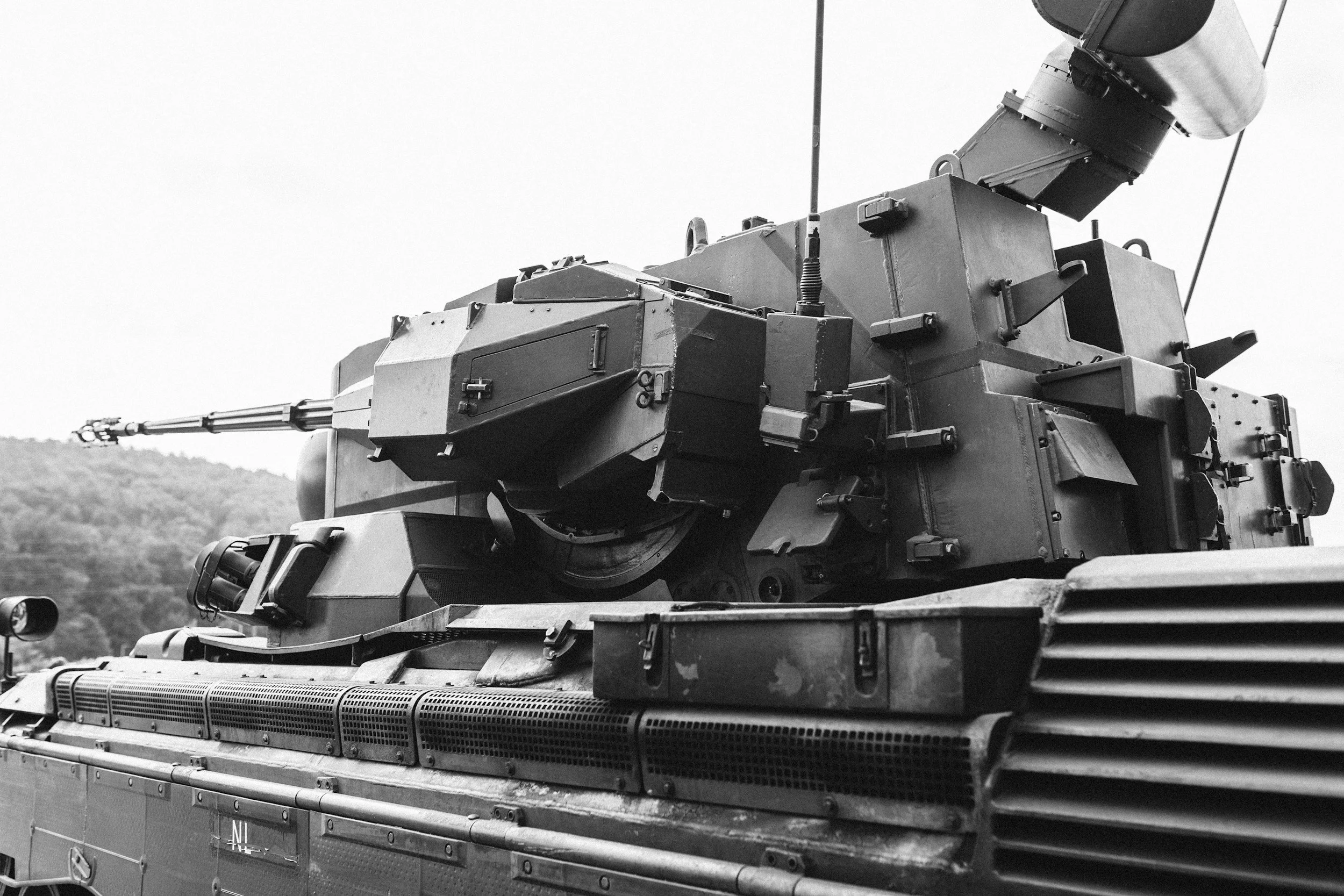 Black and white photo of a military tank with a long barrel, parked outdoors with hills in the background.