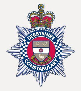 Badge of Derbshire Constabulary featuring a crown, a shield with a knight's helmet, three symbols, and a blue and white checkered pattern, with a silver starburst background.