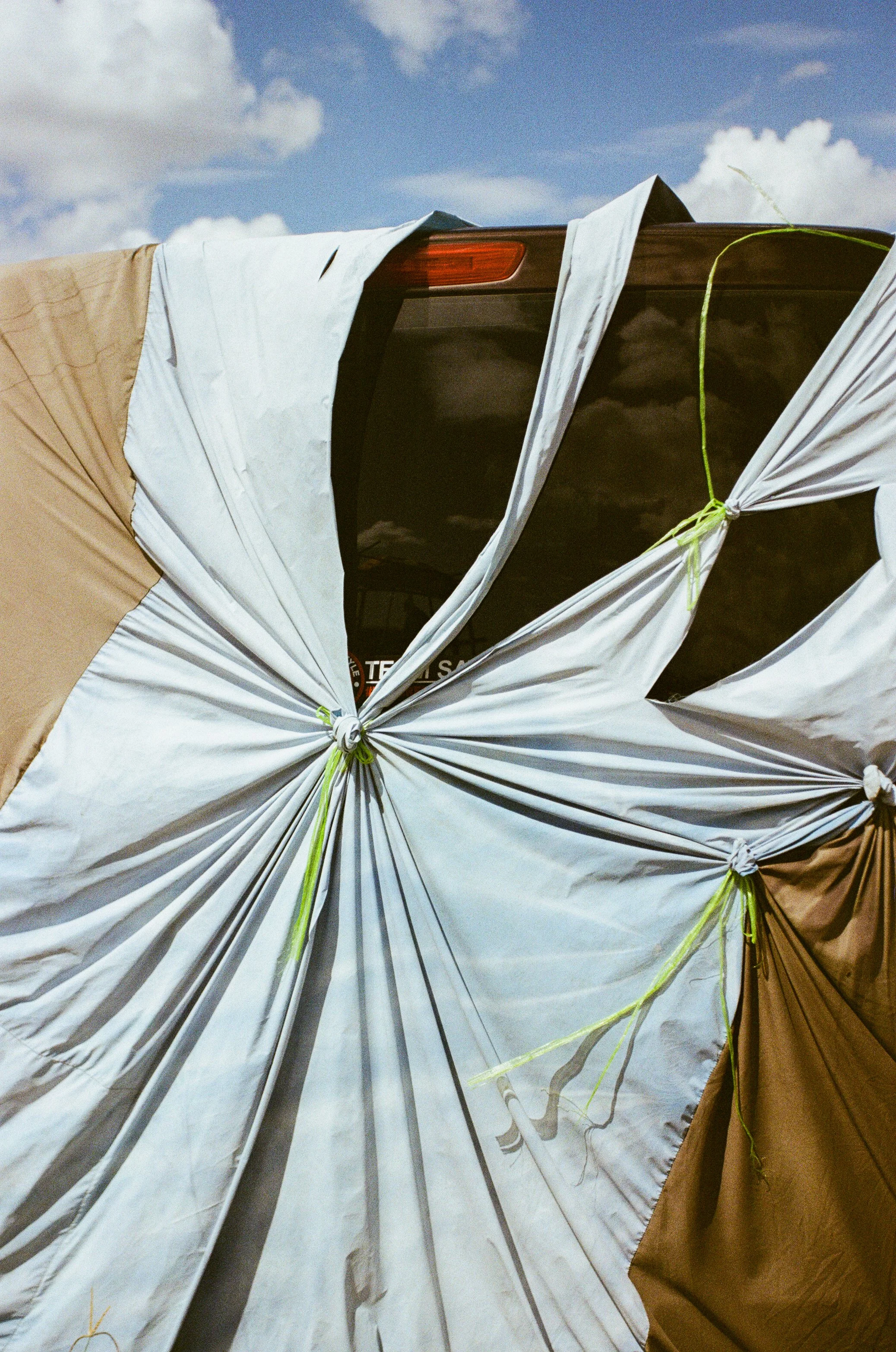 Tents with fabric tied down with green ropes set up outdoors under a partly cloudy sky.