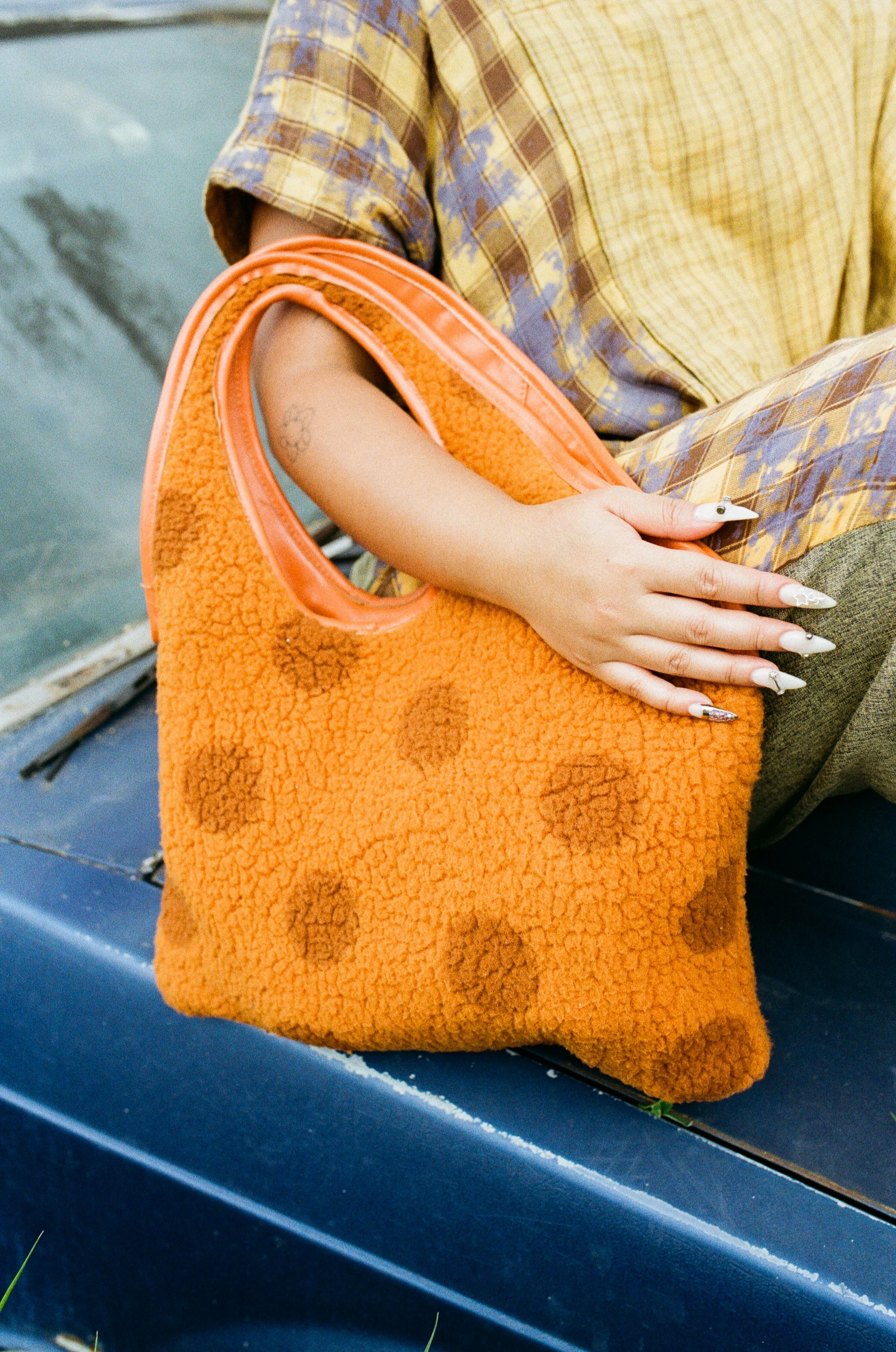 Close-up of a person's hand holding an orange terry cloth bag with a cutout handle, sitting on a blue surface.