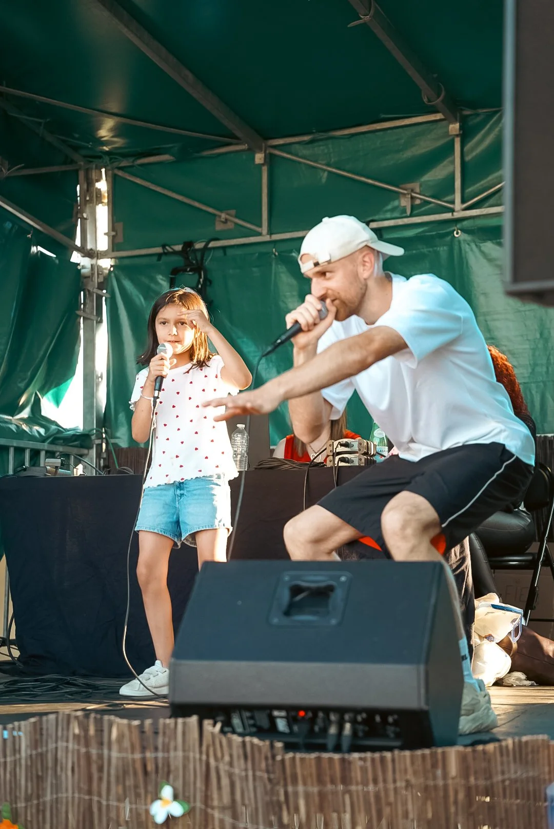 Un homme et une jeune fille chantent avec des microphones sur une scène durant un spectacle en plein air.