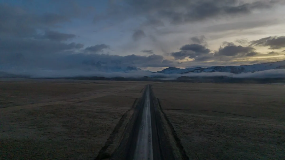 A straight railway track running through a vast open field under a cloudy sky during twilight.
