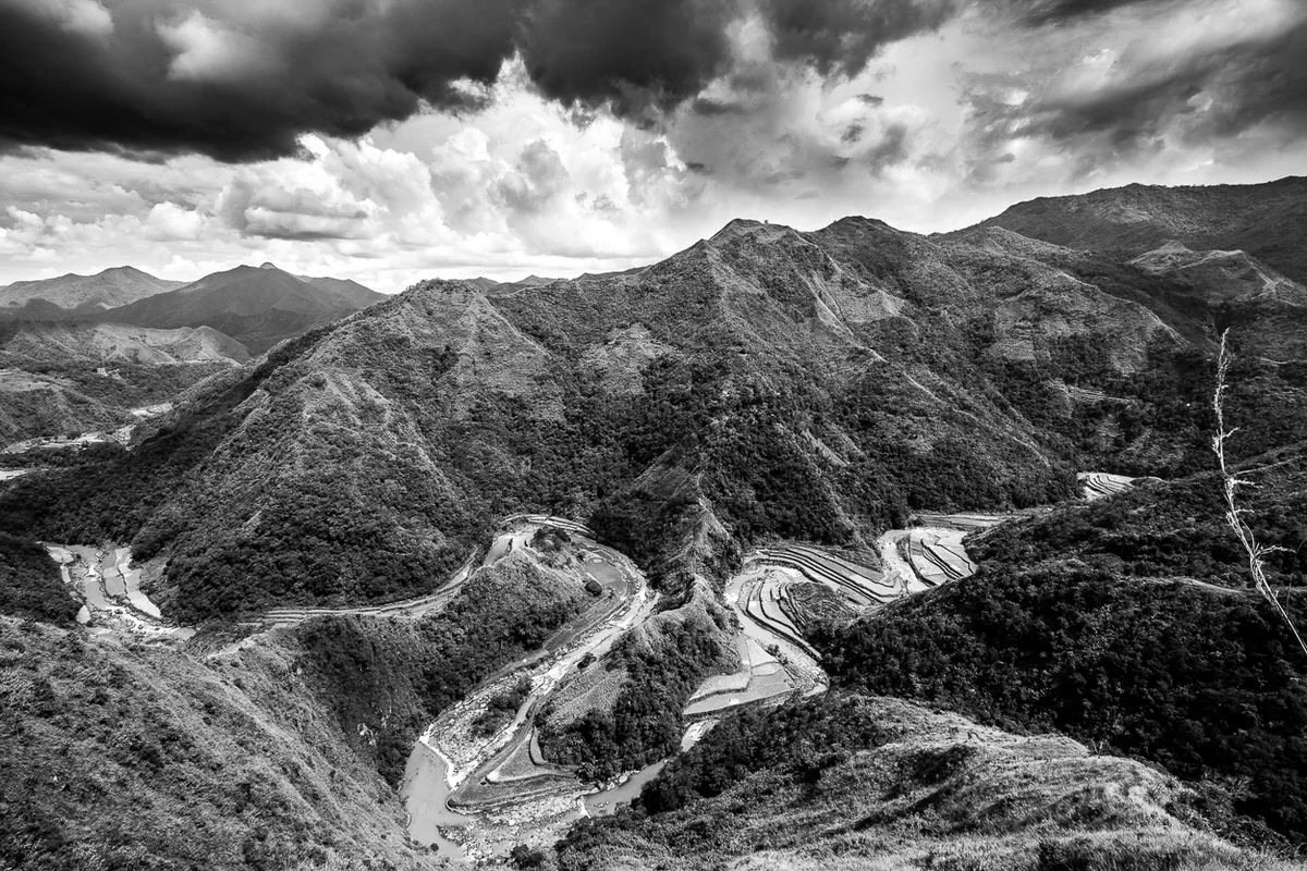 Black and white photo of a mountainous landscape with winding roads and terraced fields.