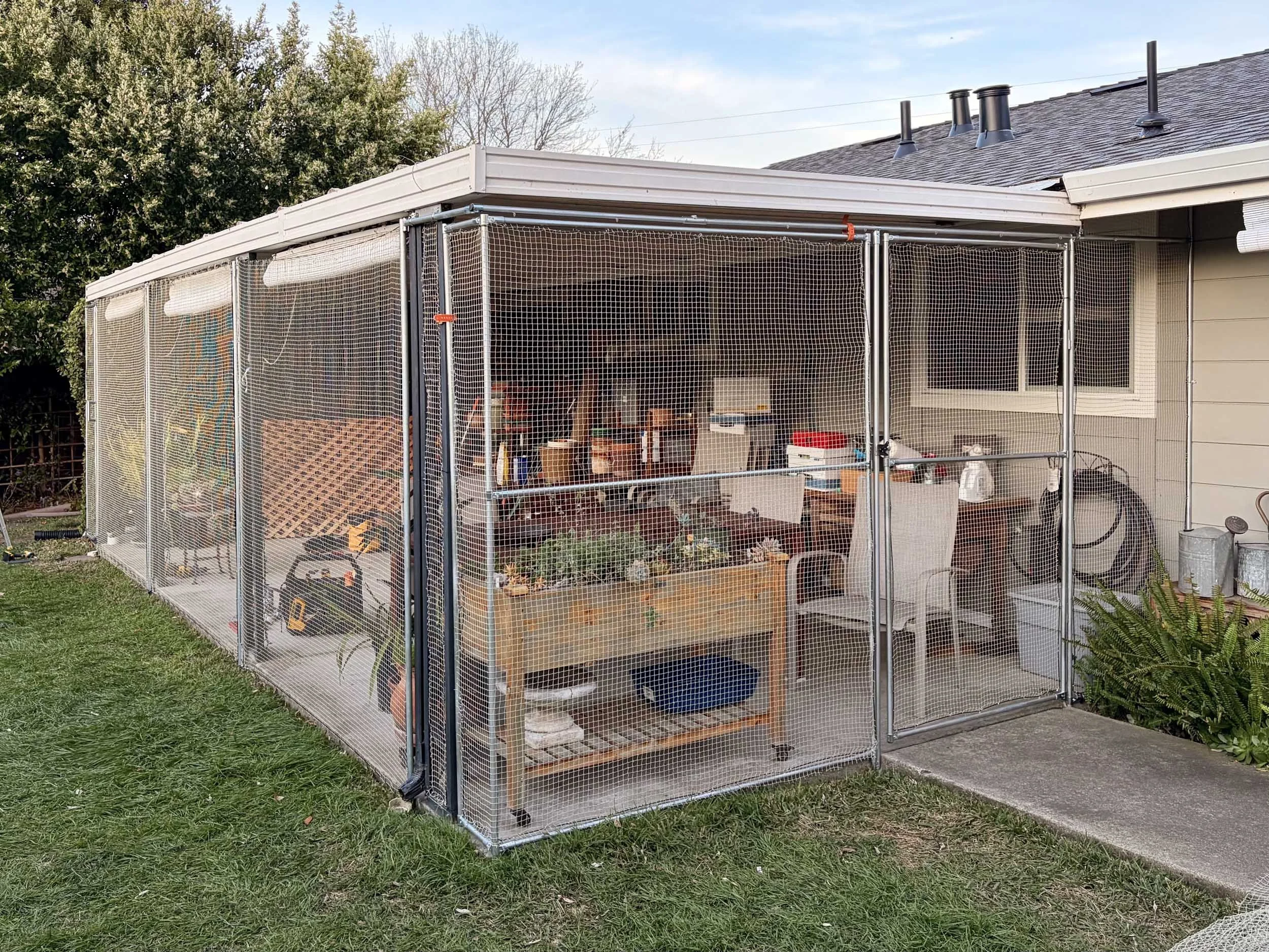 A backyard with a screened-in porch attached to a house, containing gardening tools, plant pots, and storage containers.
