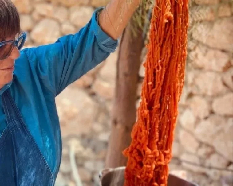 aviva in her outdoor dye kitchen holding a skein of hand spun wool dyed with madder