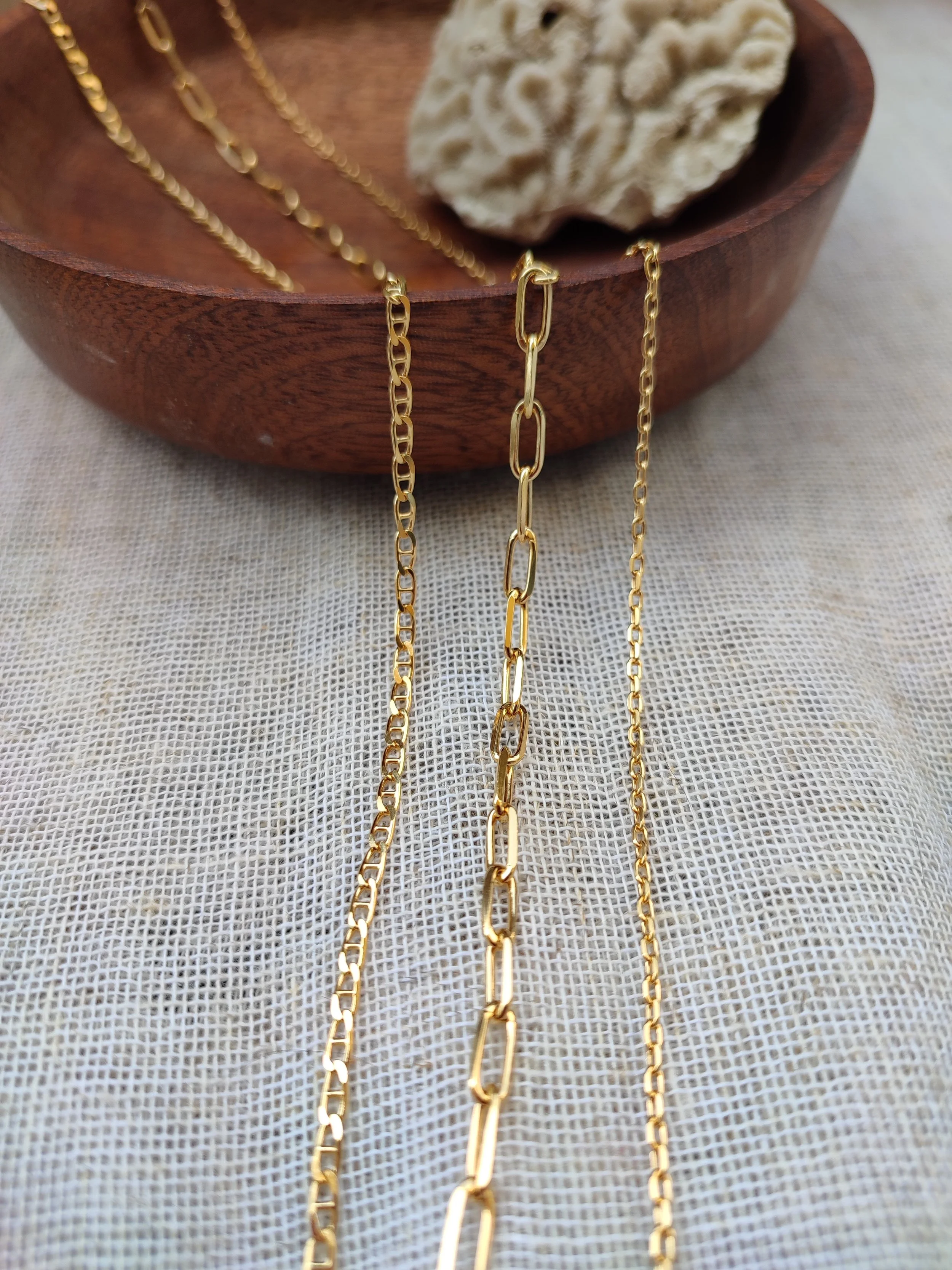 Colliers et chaines en or posés sur un tissu blanc dans un bol en bois