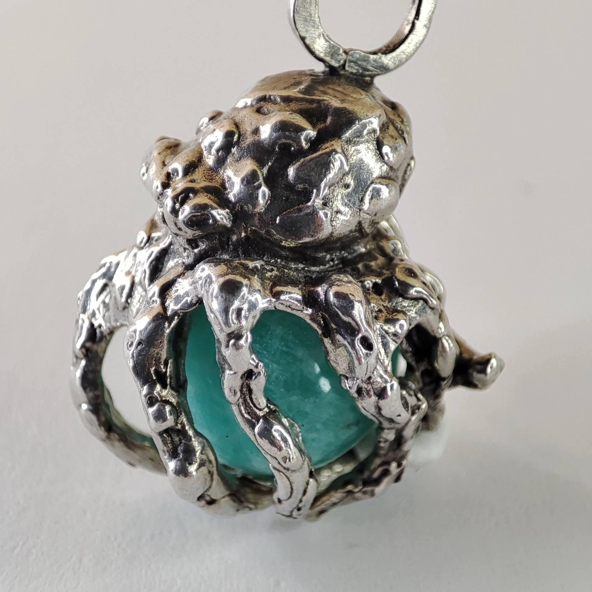 Un pendentif en argent massif 925 avec une pierre turquois au centre, représentant une pieuvre avec ses tentacules entourant la pierre.