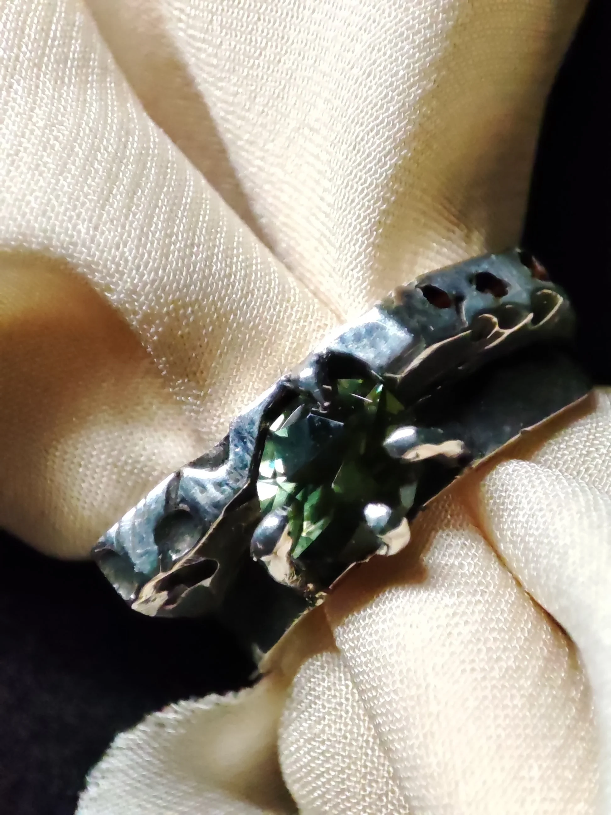 Bague en métal avec pierre précieuse verte, posée sur un tissu beige.