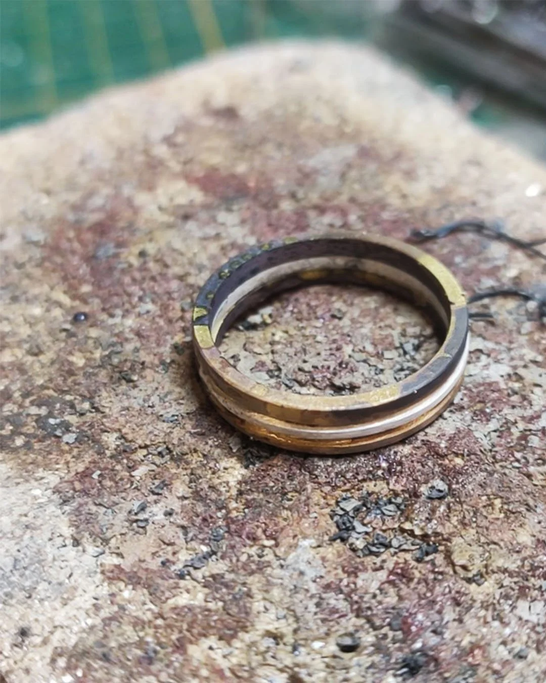 Une bague en métal précieux en phase de création, posée sur une surface de pierre ou de béton. Création de joaillerie WIT.
