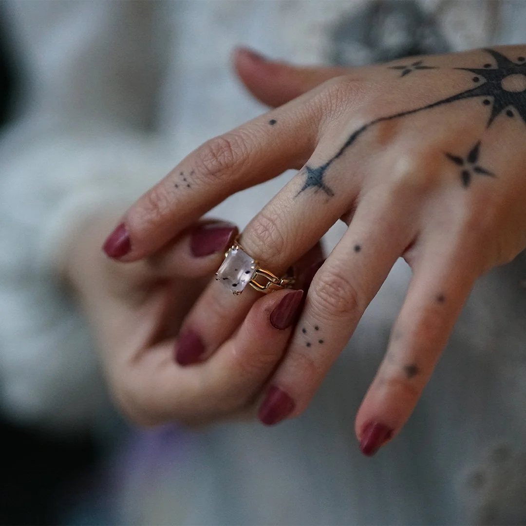 Main avec tatouages portant une bague en or avec un quartz rose à diopside.