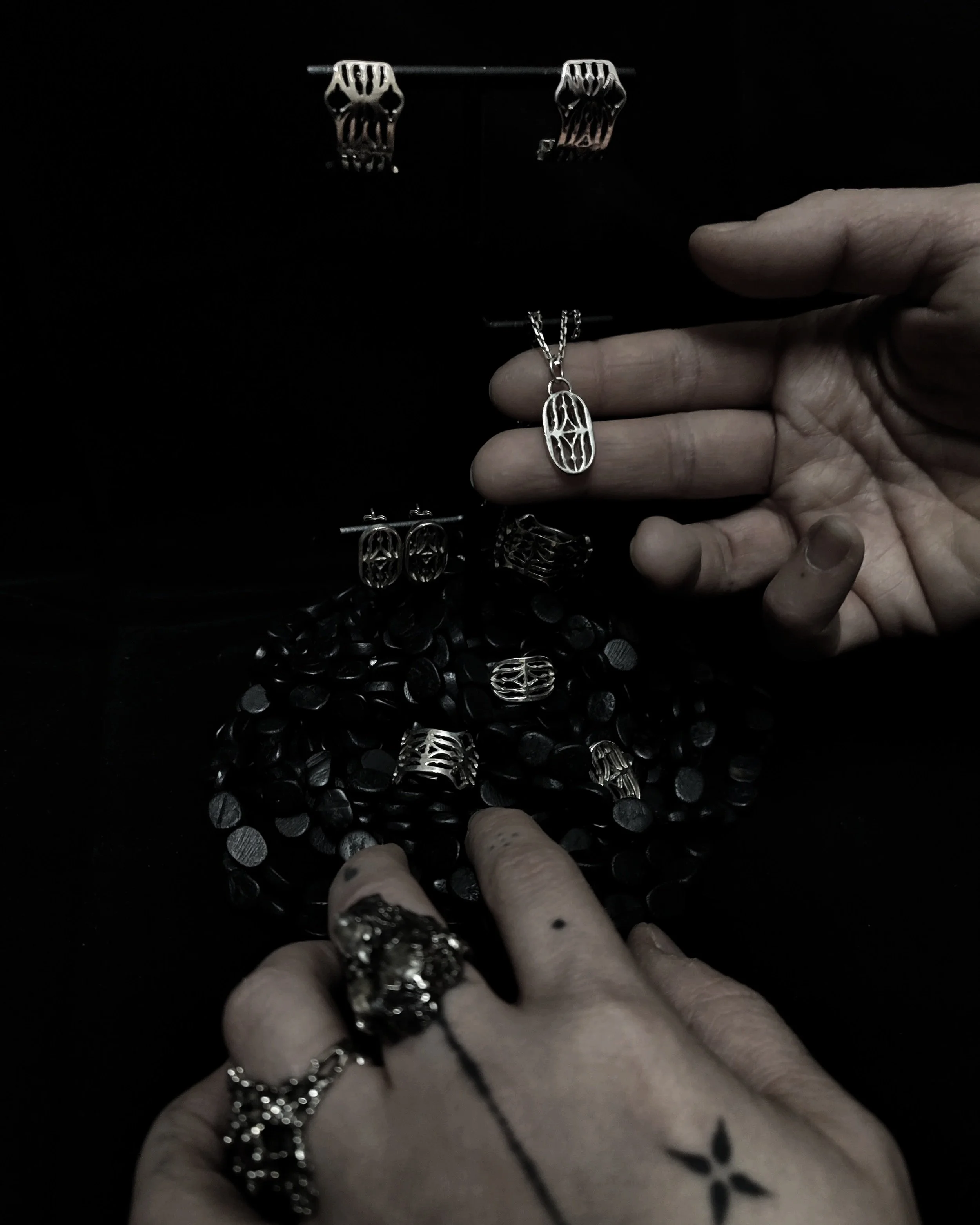 Mains présentant la collection Cluny en argent massif 925 sur fond sombre. Inspiration d'après le musée du moyen-âge, design intemporel et raffiné.