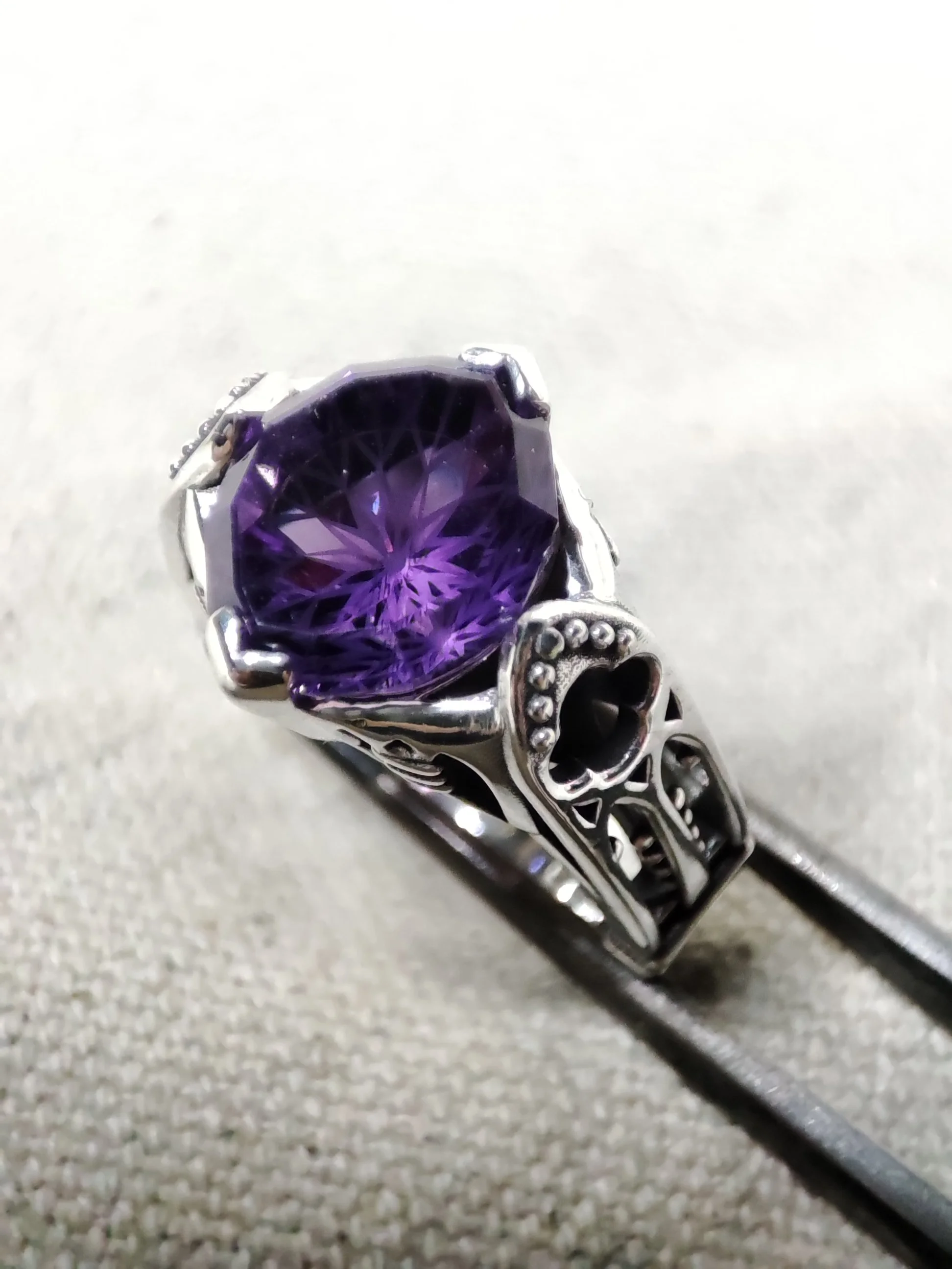 Bague notre-dame en argent avec une grande pierre violette facettée, amethyste, entourée de détails décoratifs gothiques en argent.