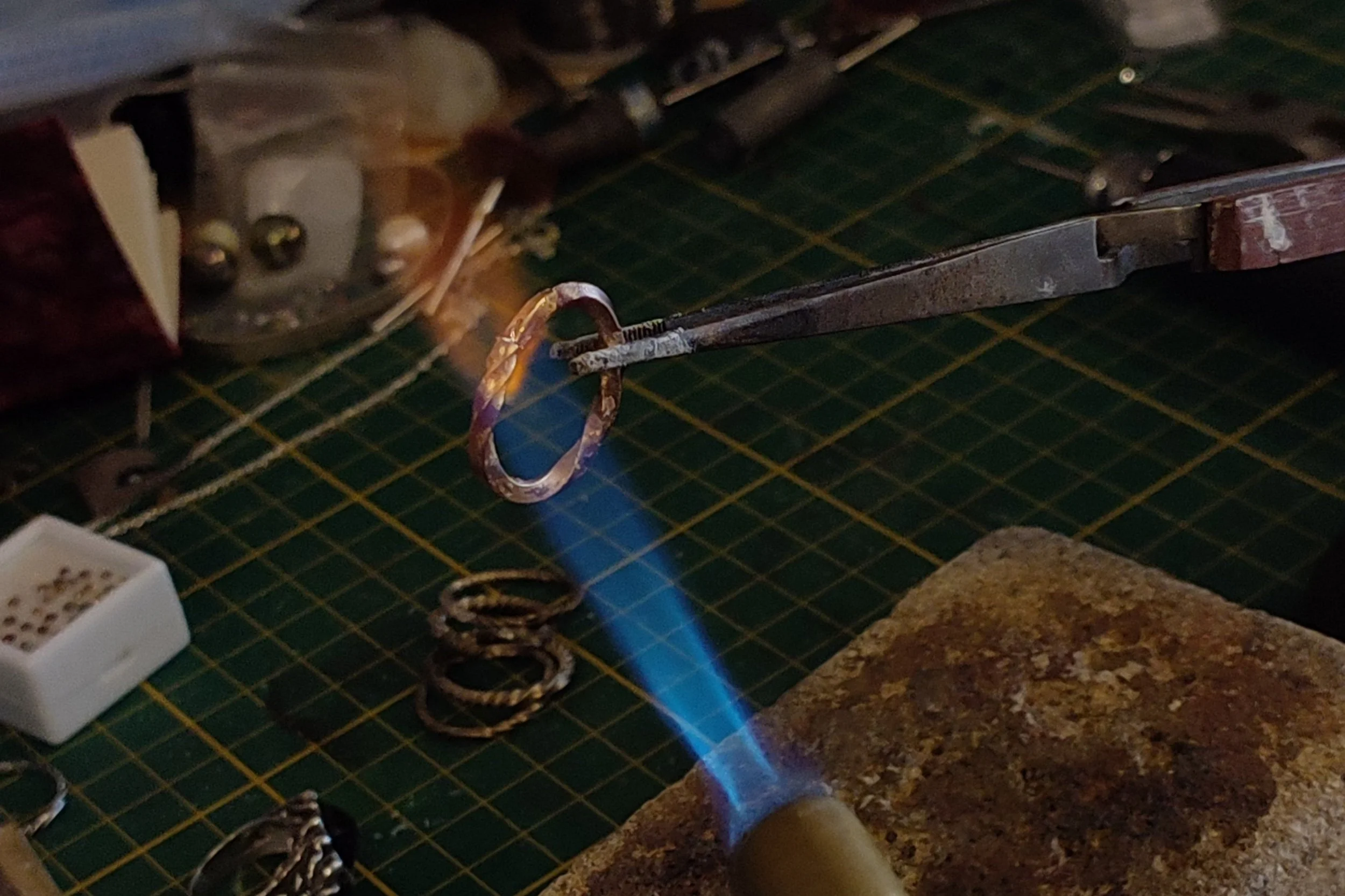 Création d'une bague. Anneau tenu par une pince et chauffé au chalumeau sur un plan de travail
