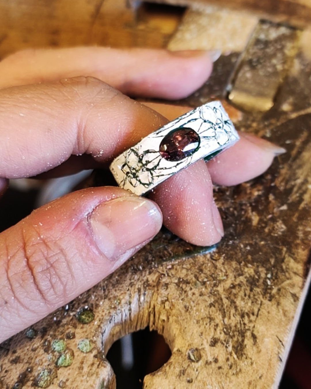 Une main tenant une bague en or avec une pierre précieuse sombre, posée sur une surface en bois.