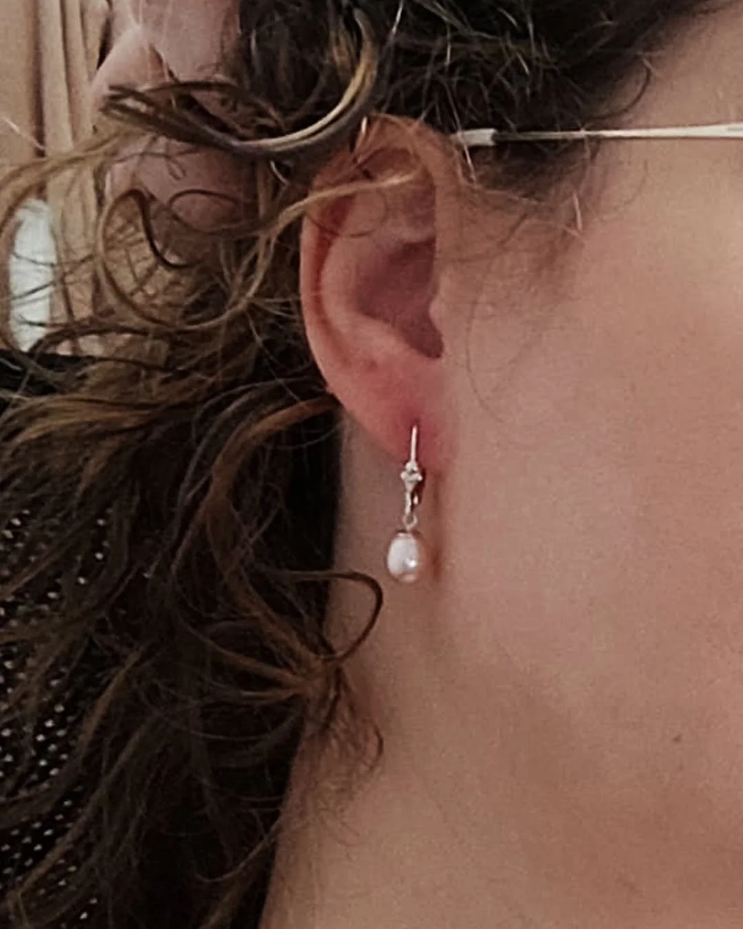 Une oreille avec un boucles d'oreilles en perle, entourée de cheveux ondulés.