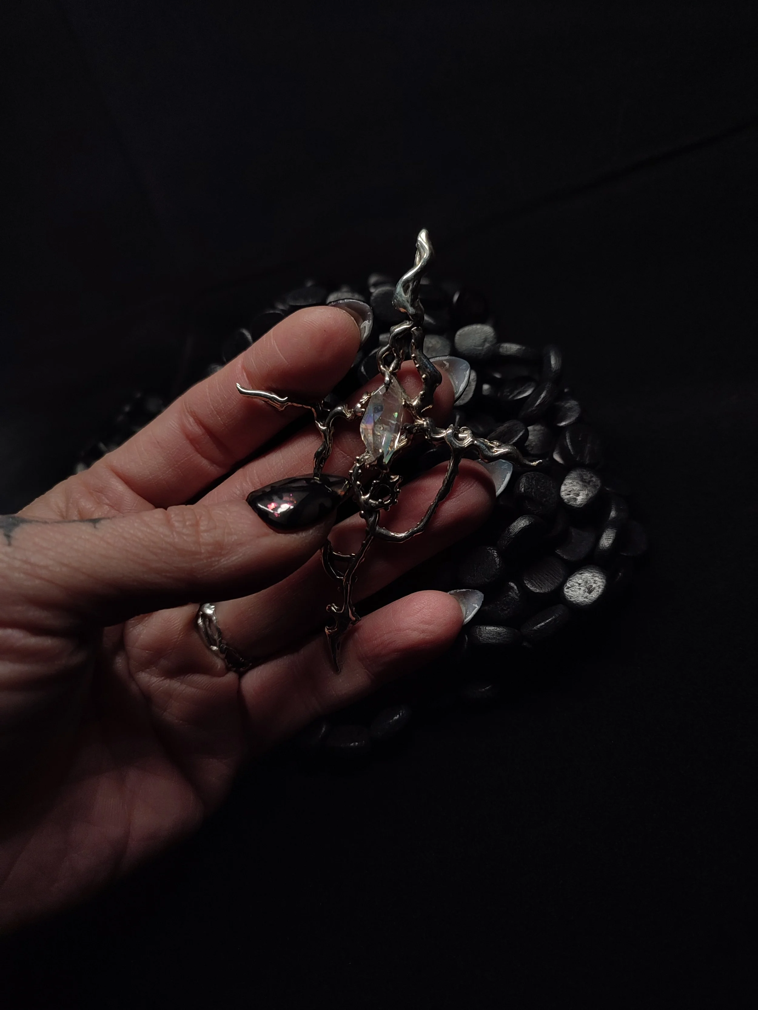 Une main tenant un bijou en forme de croix en argent massif avec des cristaux, posé sur un fond noir.