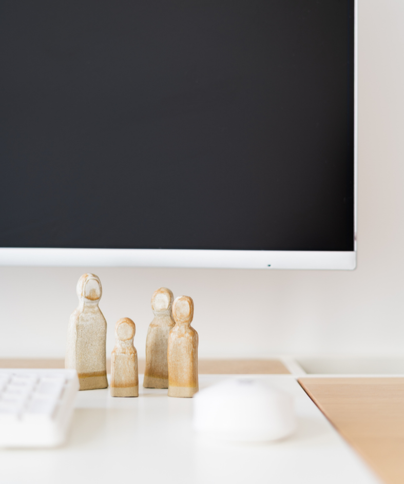 Wooden figurines of a family placed on a desk in front of a computer monitor.