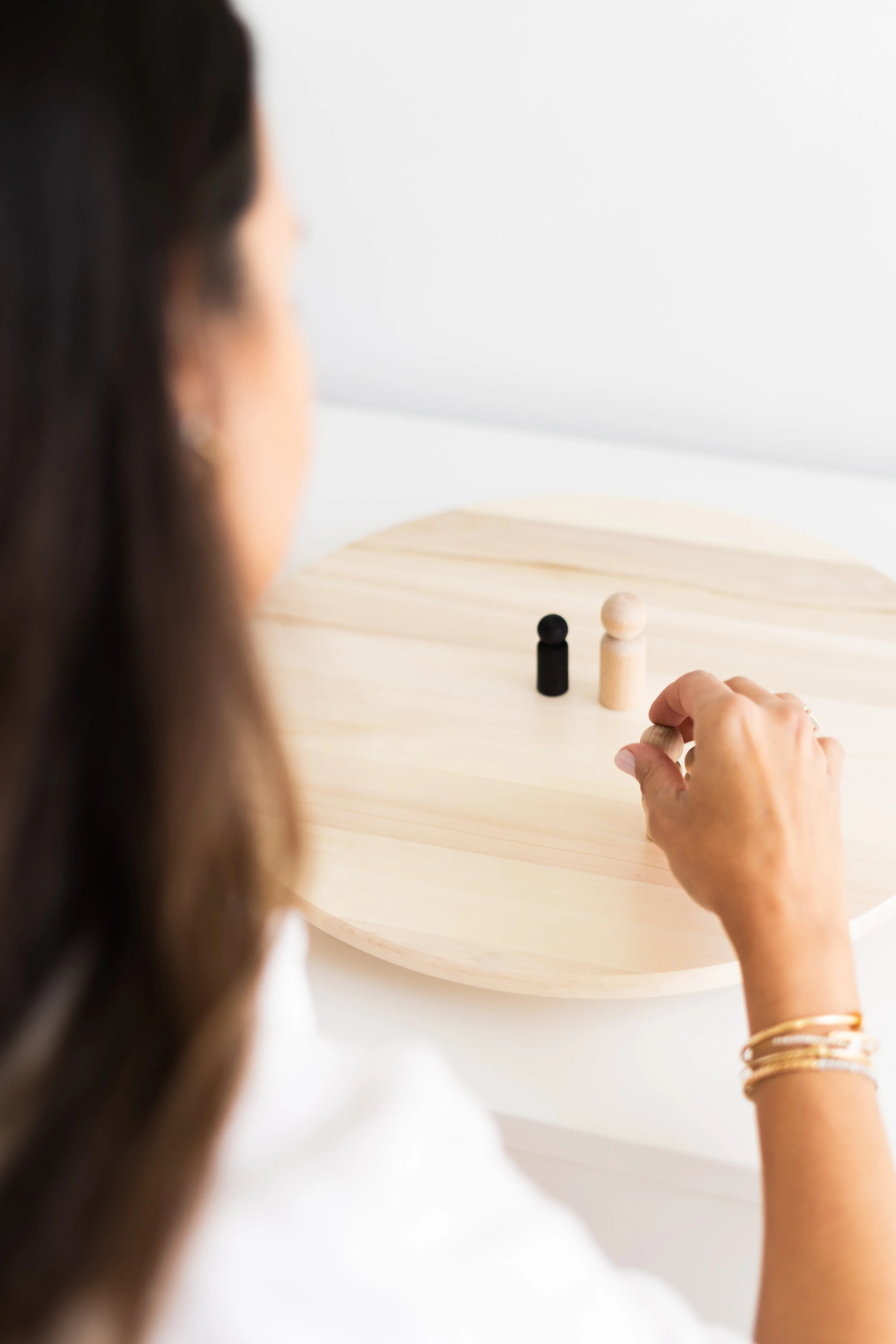 A woman with brown hair playing a game of peg solitaire with wooden pegs on a large round wooden board.