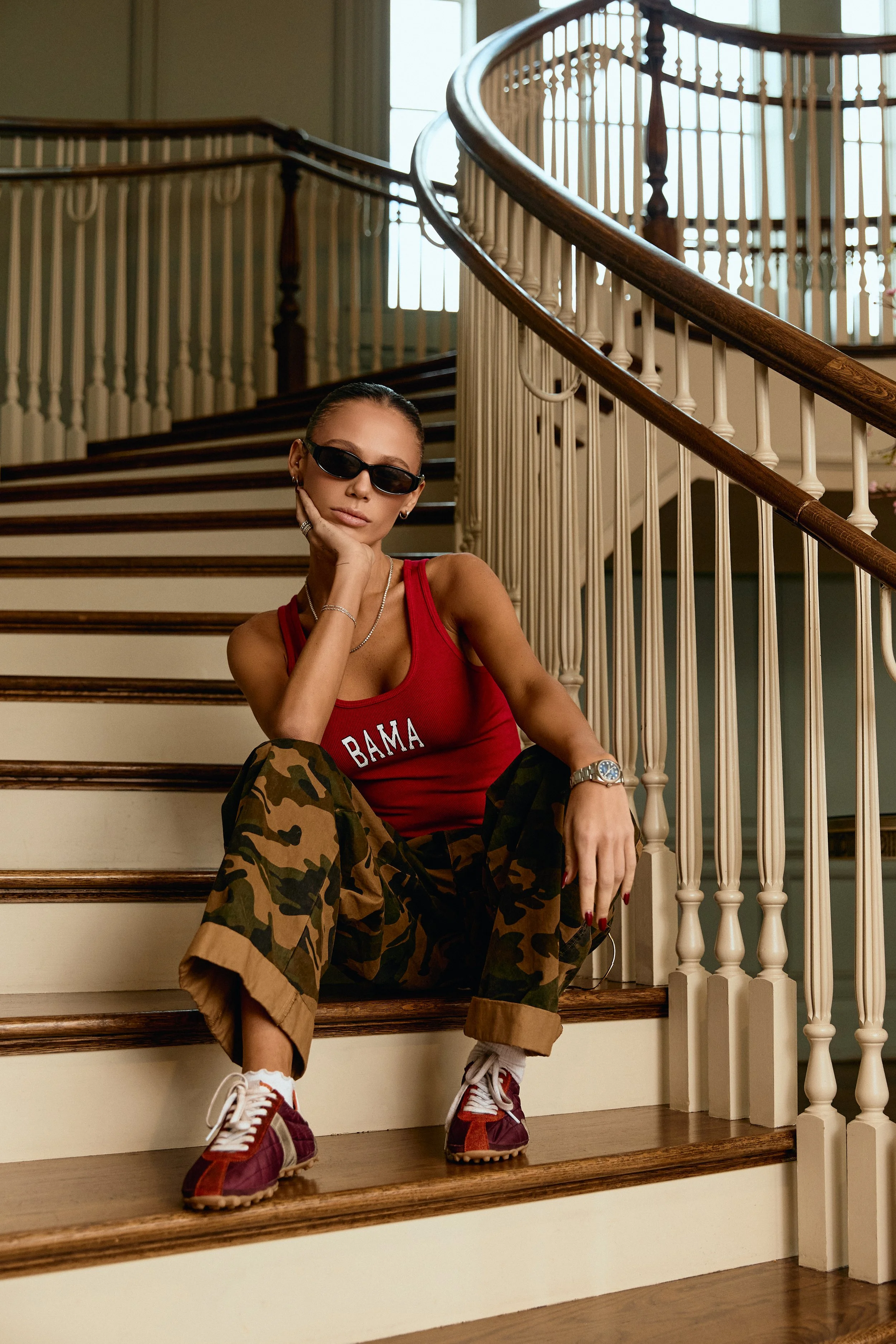 Hallie Betchelder wearing a red Bama tank and camo pants, sitting on a grand staircase.